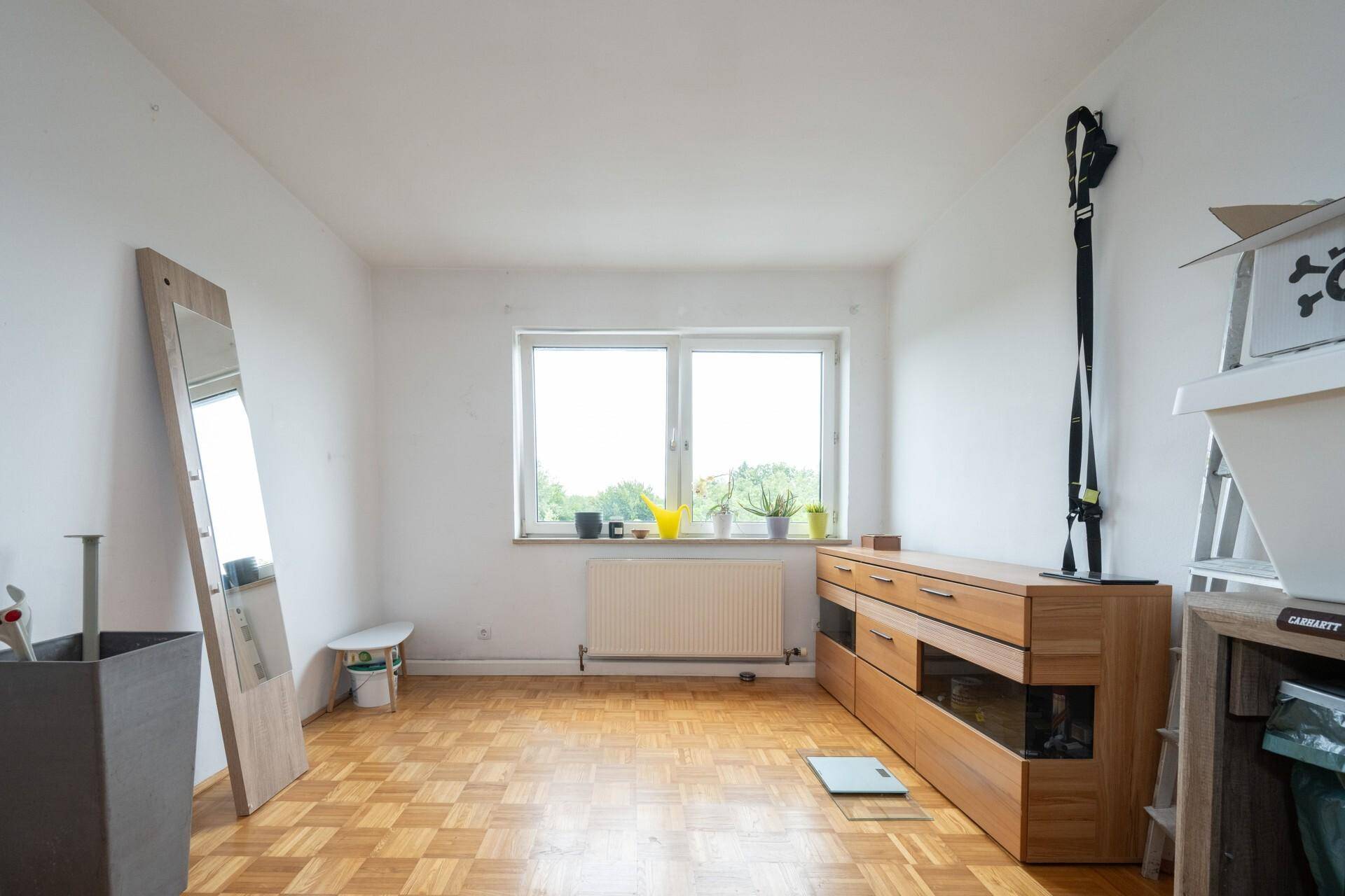Helles Zimmer mit Parkettboden, großem Fenster und Holzkommode, ideal als Schlaf- oder Arbeitszimmer.