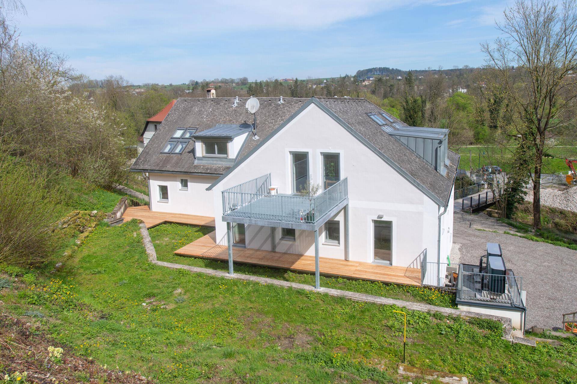 Attraktives Wohnhaus mit Balkon und Terrasse, umgeben von grüner Landschaft und Bäumen.