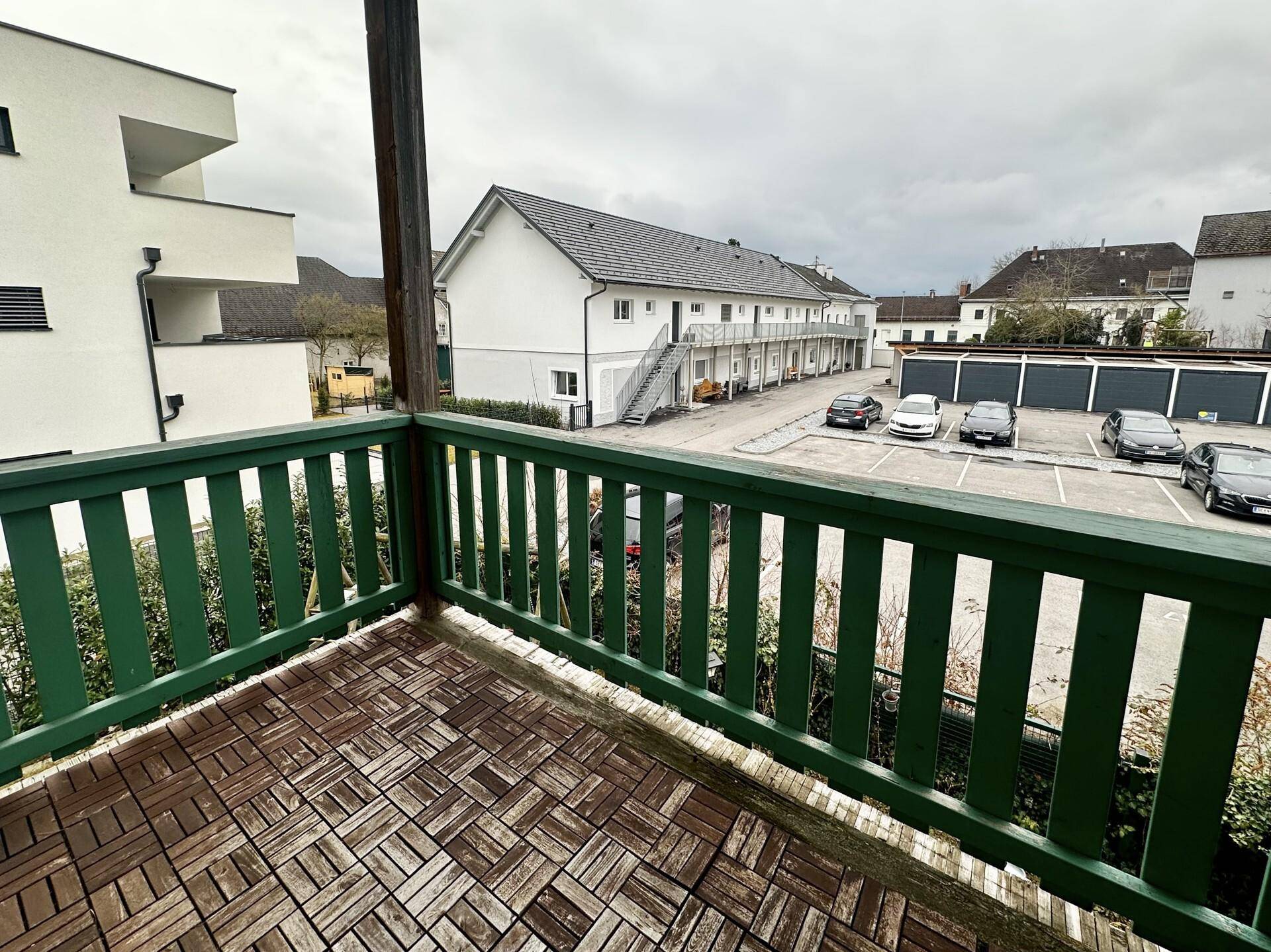 Balkon mit Holzboden und Blick auf den Parkplatz und umliegende Gebäude.