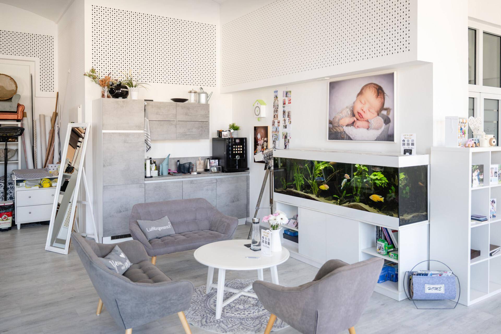 Moderner Loungebereich mit integrierter Küchenzeile, bequemen Sitzgelegenheiten und einem großen Aquarium.