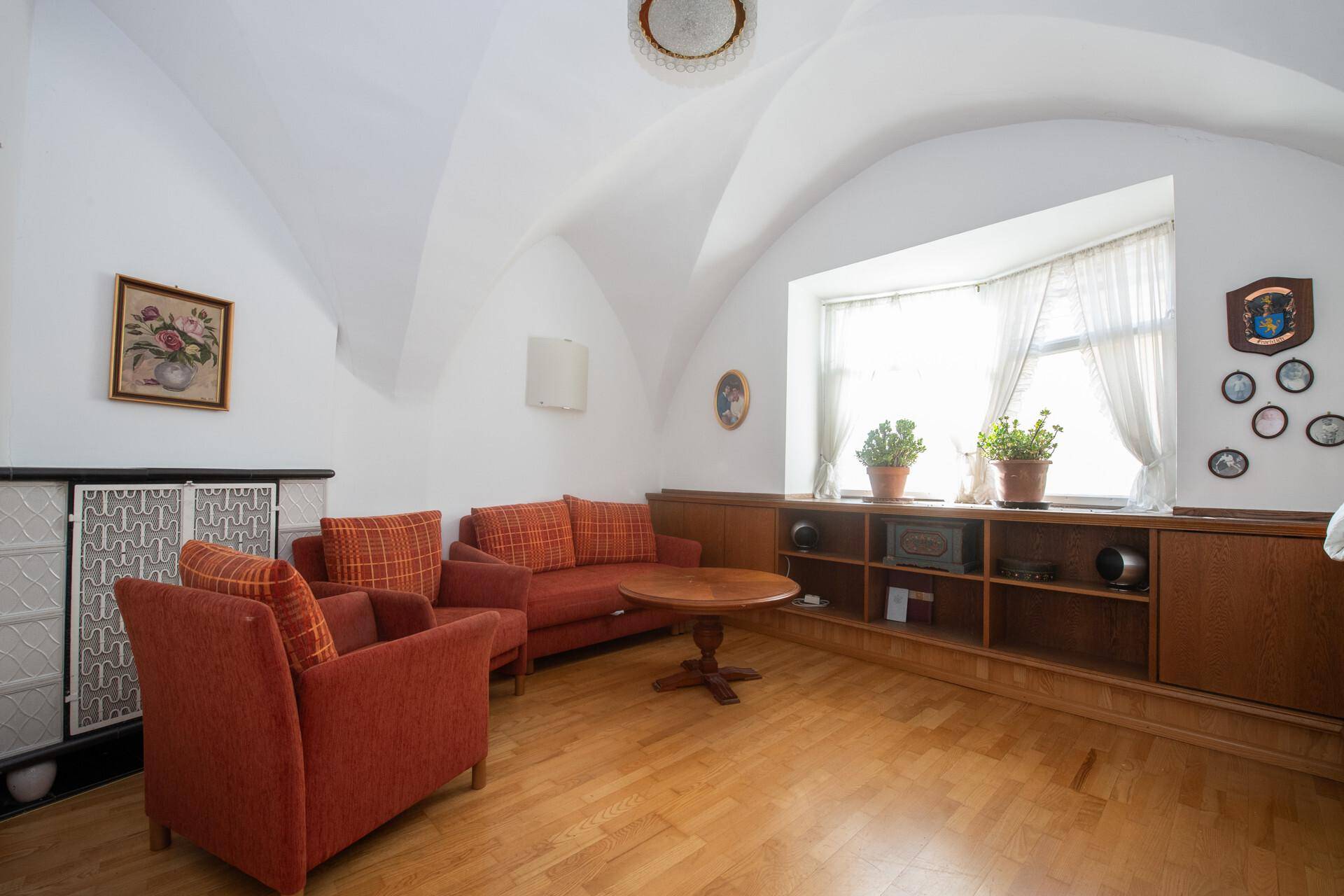Gemütliches Wohnzimmer mit Gewölbedecke, Parkettboden und einem traditionellen Kachelofen.