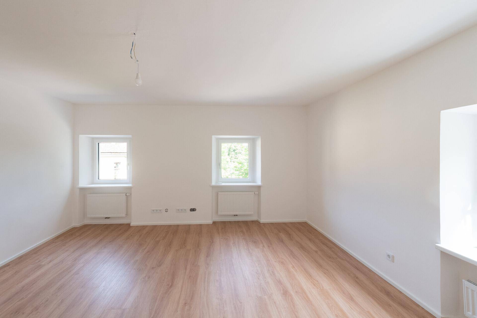 Heller, leerer Raum mit Laminatboden und mehreren Fenstern, vielseitig nutzbar.