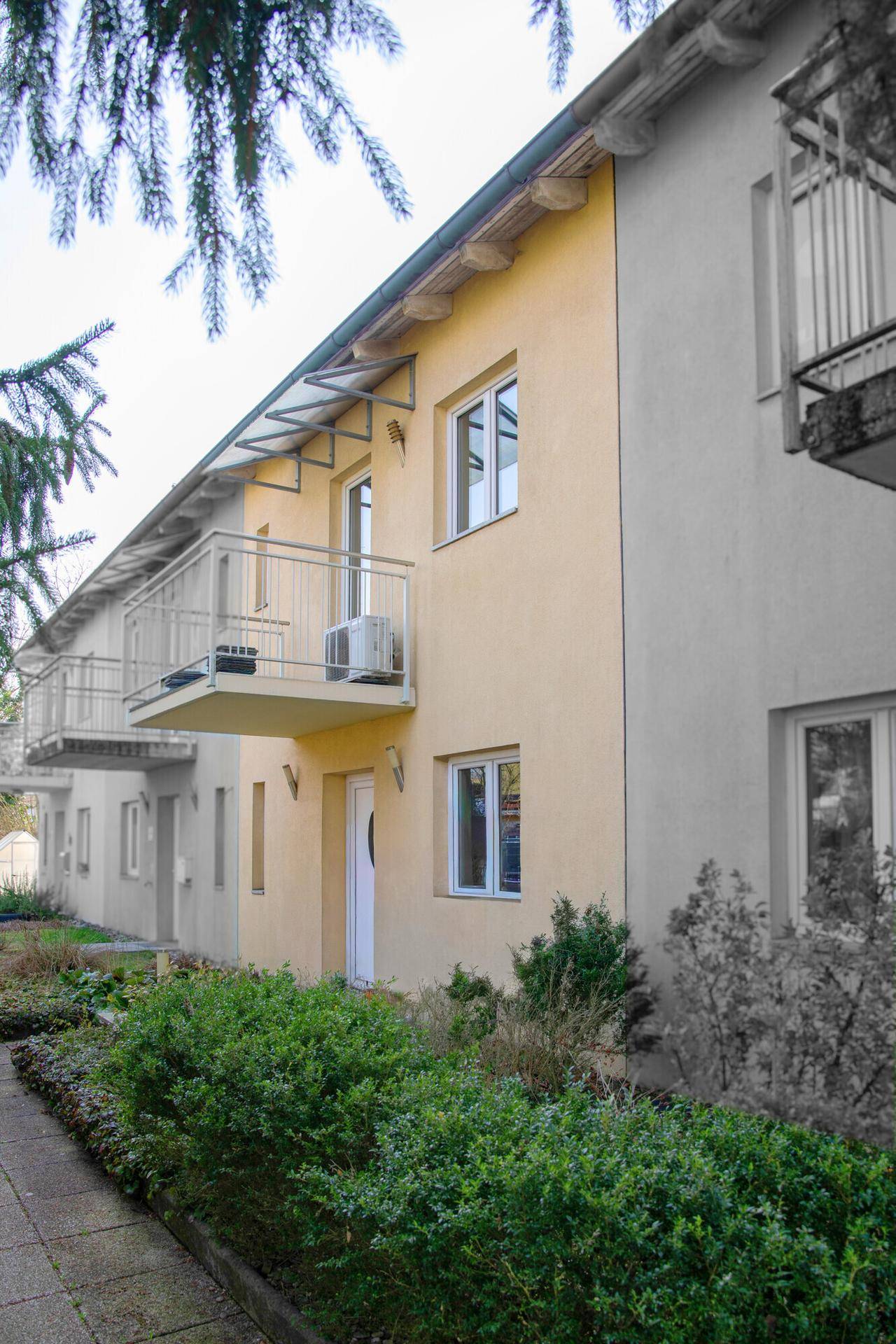 Fassade eines Mehrfamilienhauses mit Balkonen und gepflegter Vorgartenbepflanzung.