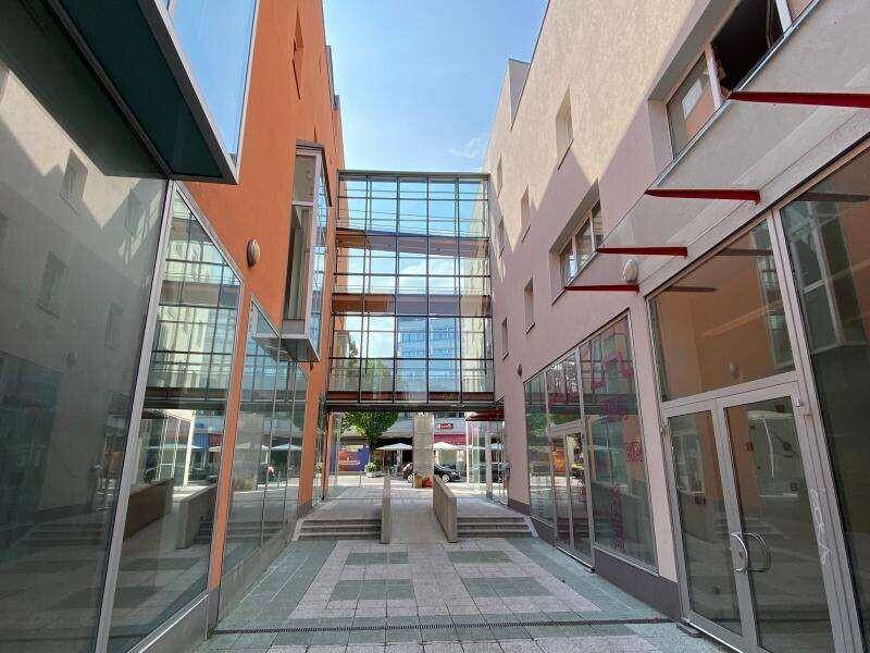 Moderne Architektur mit Glasbrücke, die zwei Gebäude verbindet, und einem gepflasterten Durchgang.