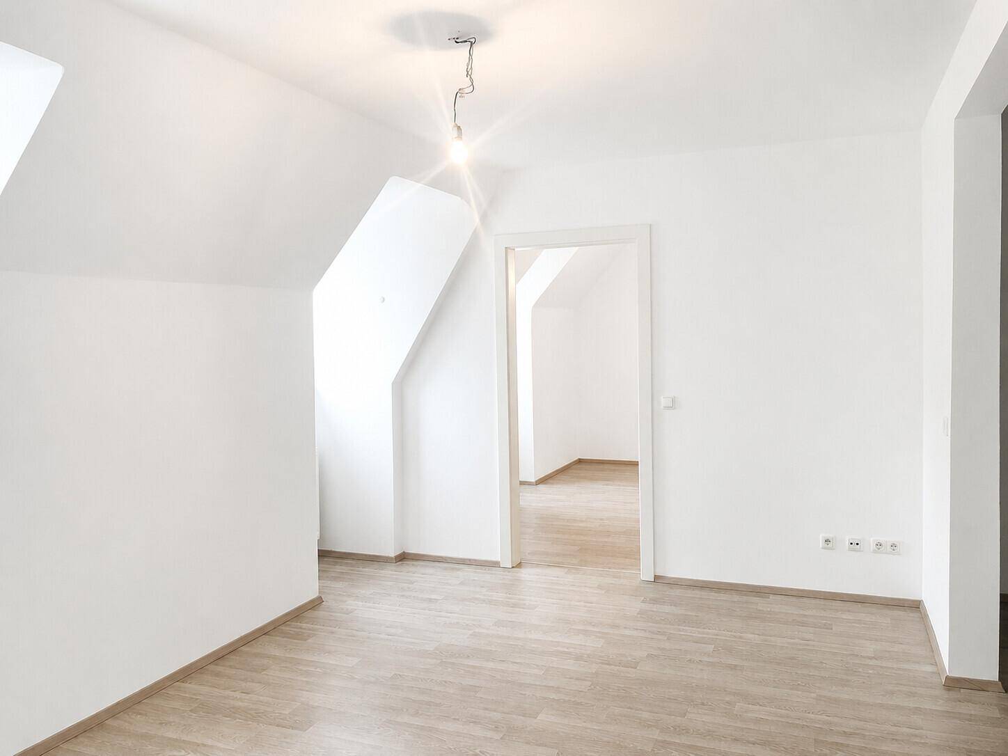 Heller, leerer Raum mit Dachschrägen und Laminatboden, der vielseitig genutzt werden kann.