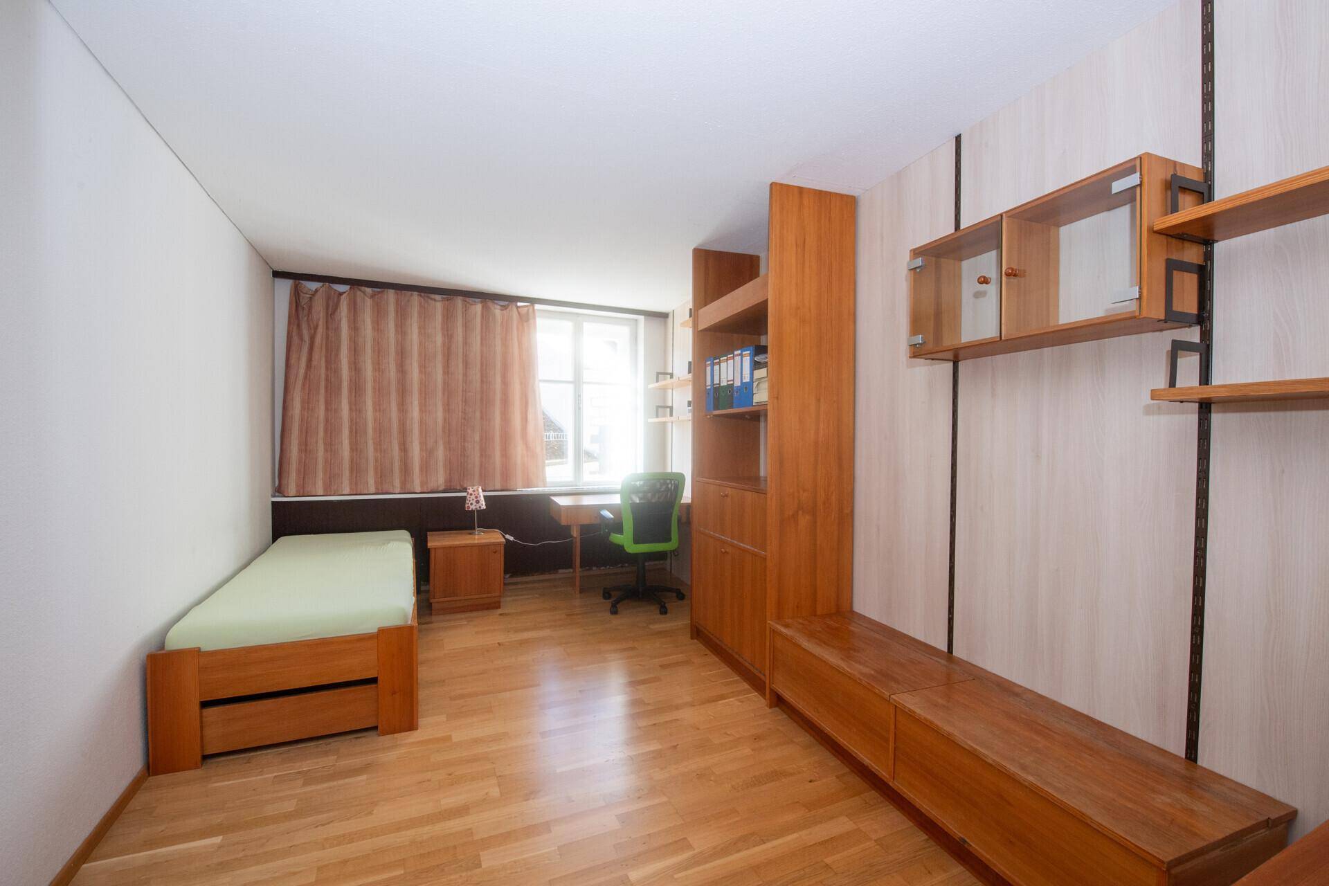 Helles Schlafzimmer mit Einzelbett, Holzmöbeln, Schreibtisch und Parkettboden, ideal als Gästezimmer.