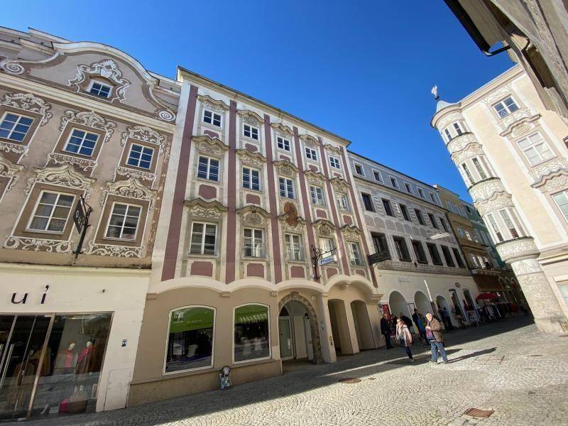 Historische Gebäudefront mit aufwendigen Verzierungen und Geschäften im Erdgeschoss an einer gepflasterten Straße.