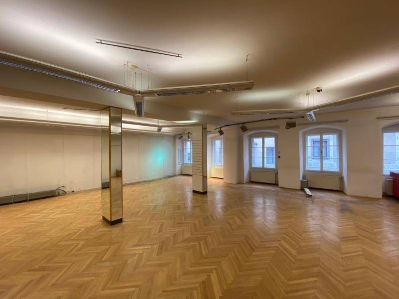 Geräumiger Gewerberaum mit Fischgrätparkett, Spiegeln und mehreren Fenstern, gut beleuchtet.