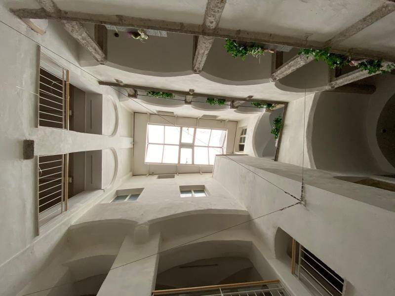 Blick nach oben in einen hellen Innenhof mit Arkaden, Pflanzen und einem großen Dachfenster.