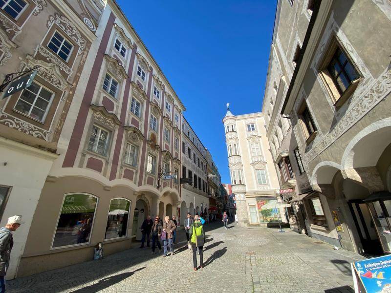 Belebte historische Straße mit Geschäften und Passanten, umgeben von alten Gebäuden mit Verzierungen.
