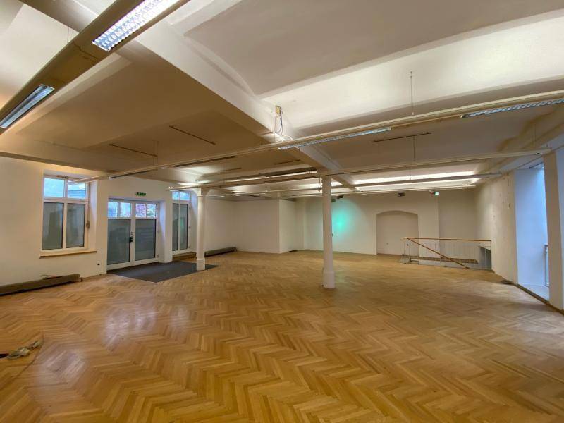 Großer, leerer Raum mit Fischgrätparkett, hohen Decken und großen Fenstern, ideal für gewerbliche Nutzung.
