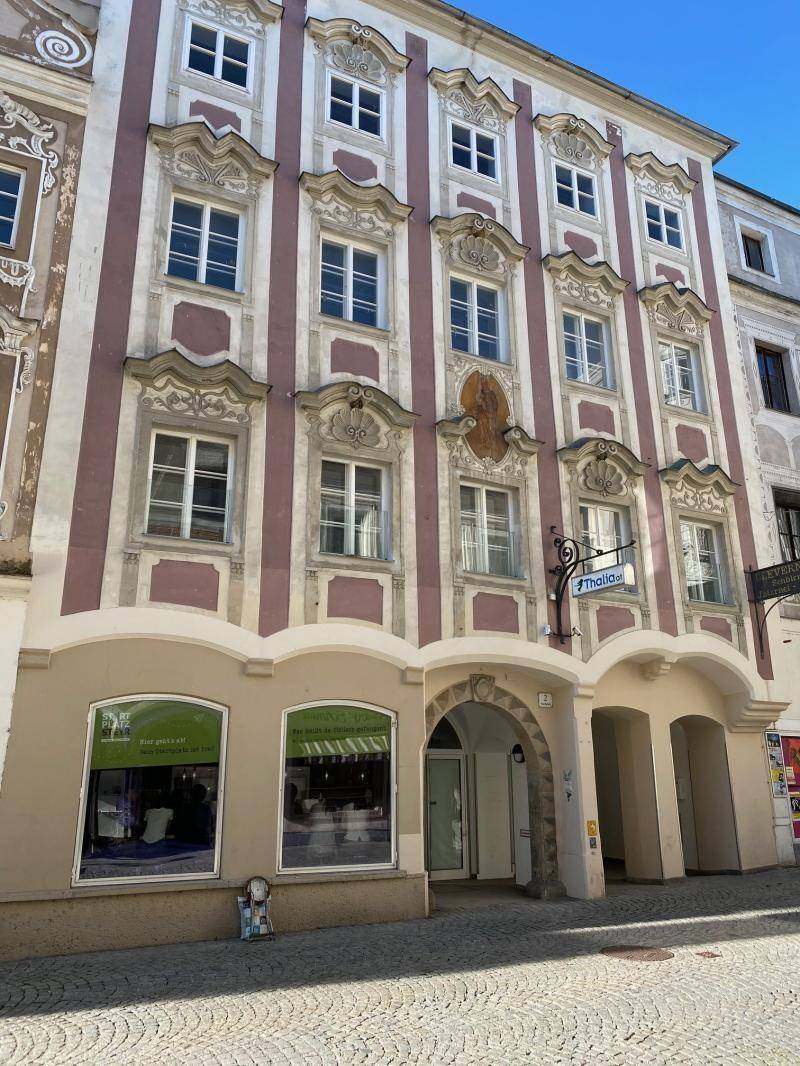 Detailansicht einer historischen Gebäudefront mit kunstvollen Verzierungen und großen Schaufenstern im Erdgeschoss.