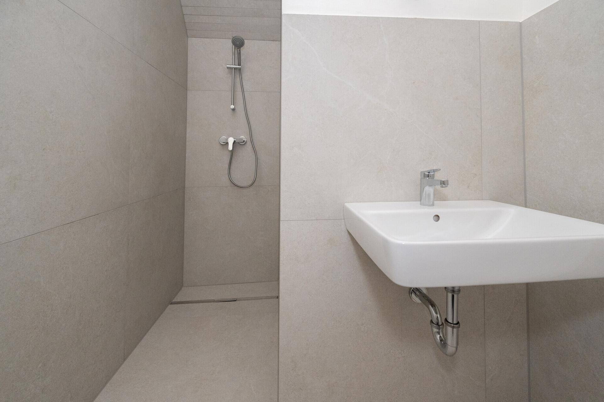 Modernes Badezimmer mit begehbarer Dusche, Waschbecken und hellen Fliesen.