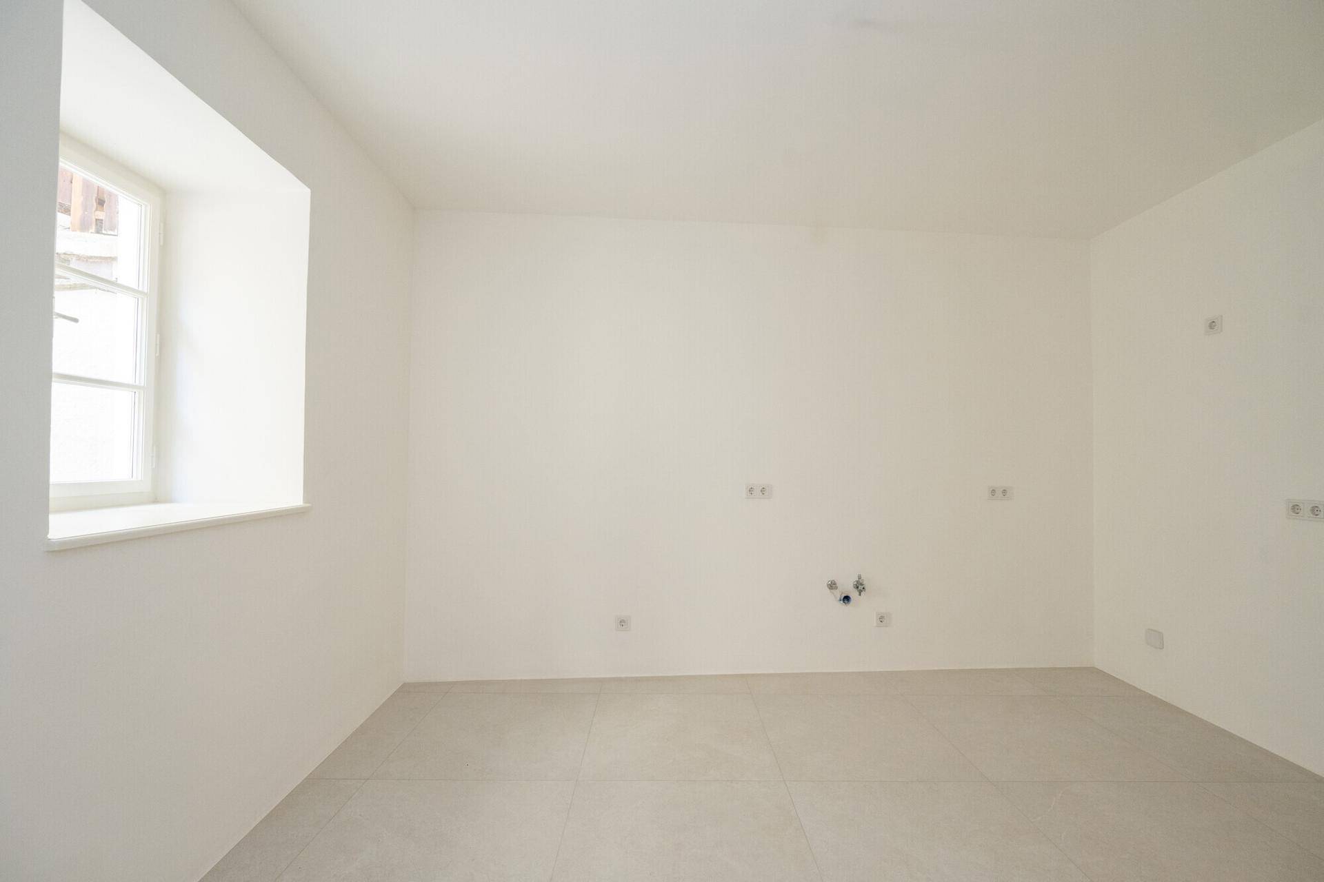 Leerer Raum mit Fliesenboden und Fenster, vorbereitet für ein Badezimmer.