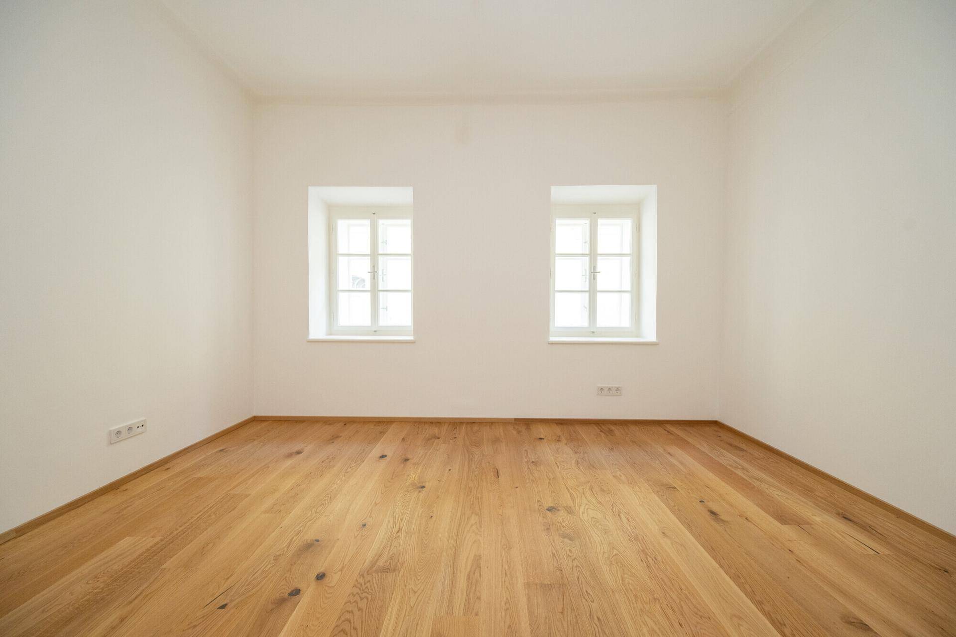 Geräumiger, heller Raum mit Holzplankenboden und zwei Fenstern, frisch renoviert und bezugsfertig.