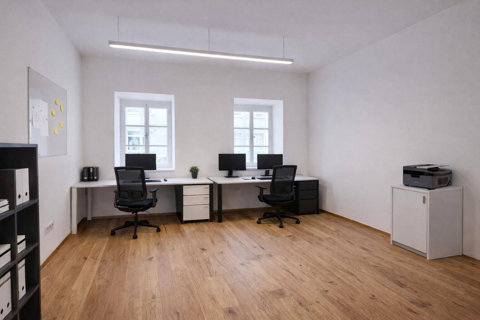 Modern eingerichtetes Büro mit zwei Arbeitsplätzen, Holzplankenboden und viel Tageslicht.