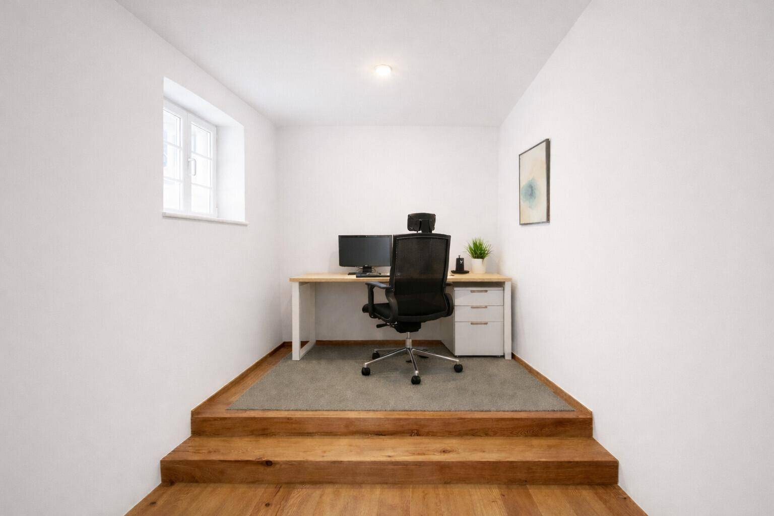 Gemütliches Büro mit Holzboden, einem Arbeitsplatz und einem kleinen Fenster, zugänglich über eine Stufe.