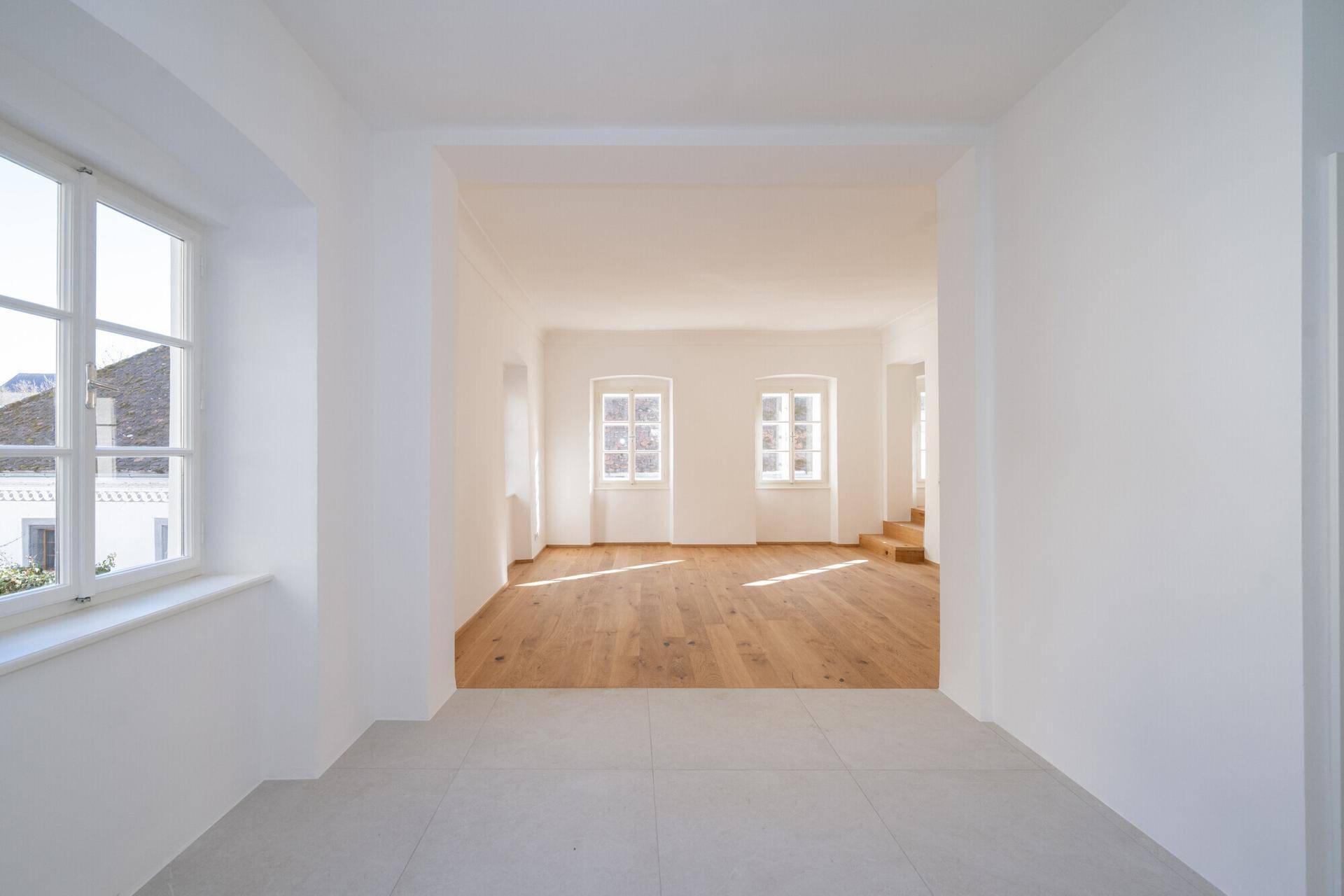 Heller Flurbereich mit Fliesenboden, der zu einem Zimmer mit Holzboden führt.