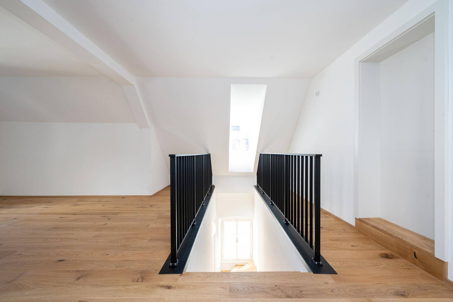 Heller Dachbodenbereich mit Holzboden und modernem schwarzem Treppengeländer.