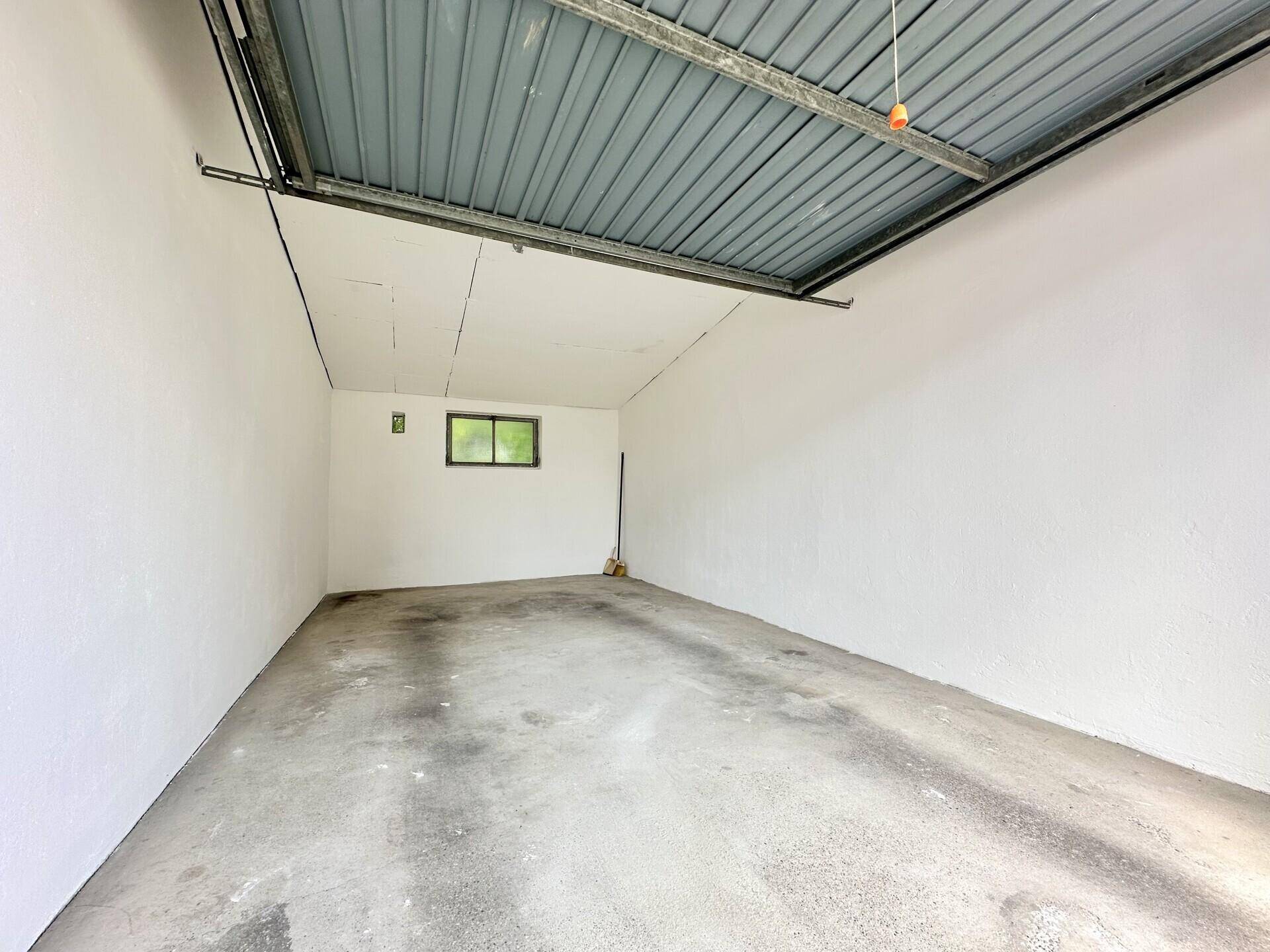 Leere Garage mit Betonboden, weiß gestrichenen Wänden und einem kleinen Fenster.