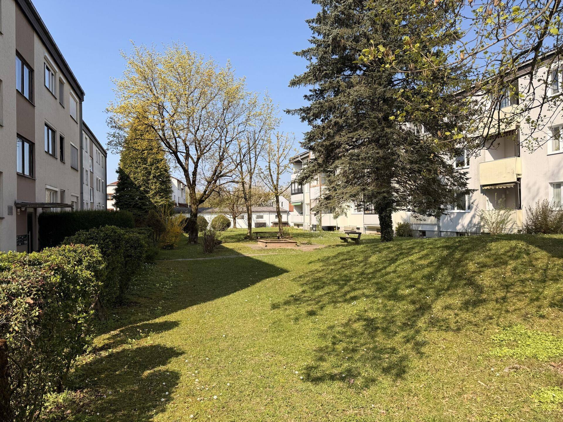 Gemeinschaftlicher Gartenbereich mit Rasenfläche, Bäumen und einem kleinen Sandkasten.