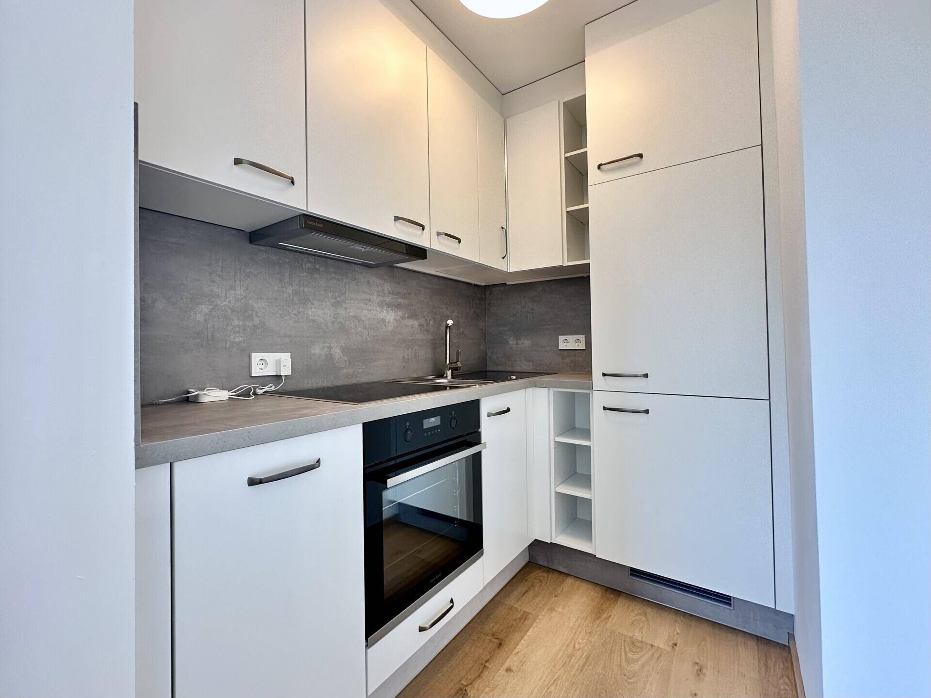 Moderne Einbauküche mit weißen Schränken, integrierten Geräten und Holzoptik-Boden.
