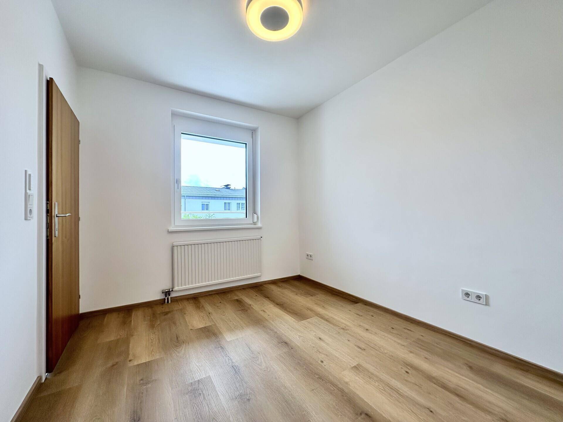 Helles Schlafzimmer mit Laminatboden, weiß gestrichenen Wänden und einem Fenster.