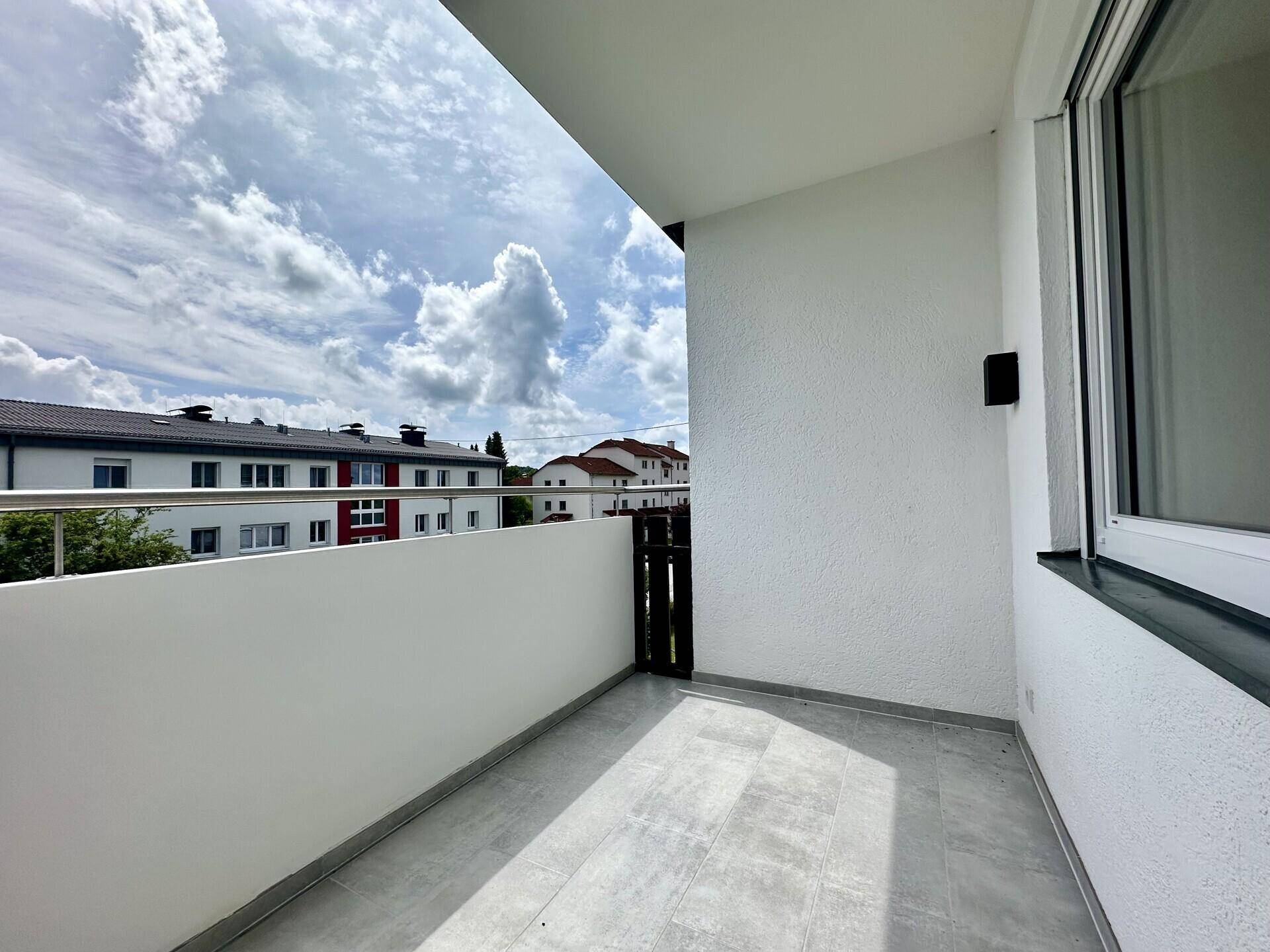 Heller Balkon mit Fliesenboden und Blick auf die umliegenden Gebäude und den Himmel.