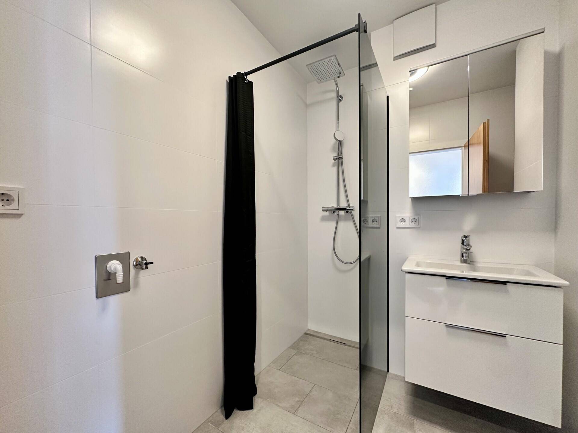Modernes Badezimmer mit begehbarer Dusche, weiß gefliesten Wänden und Waschtisch.