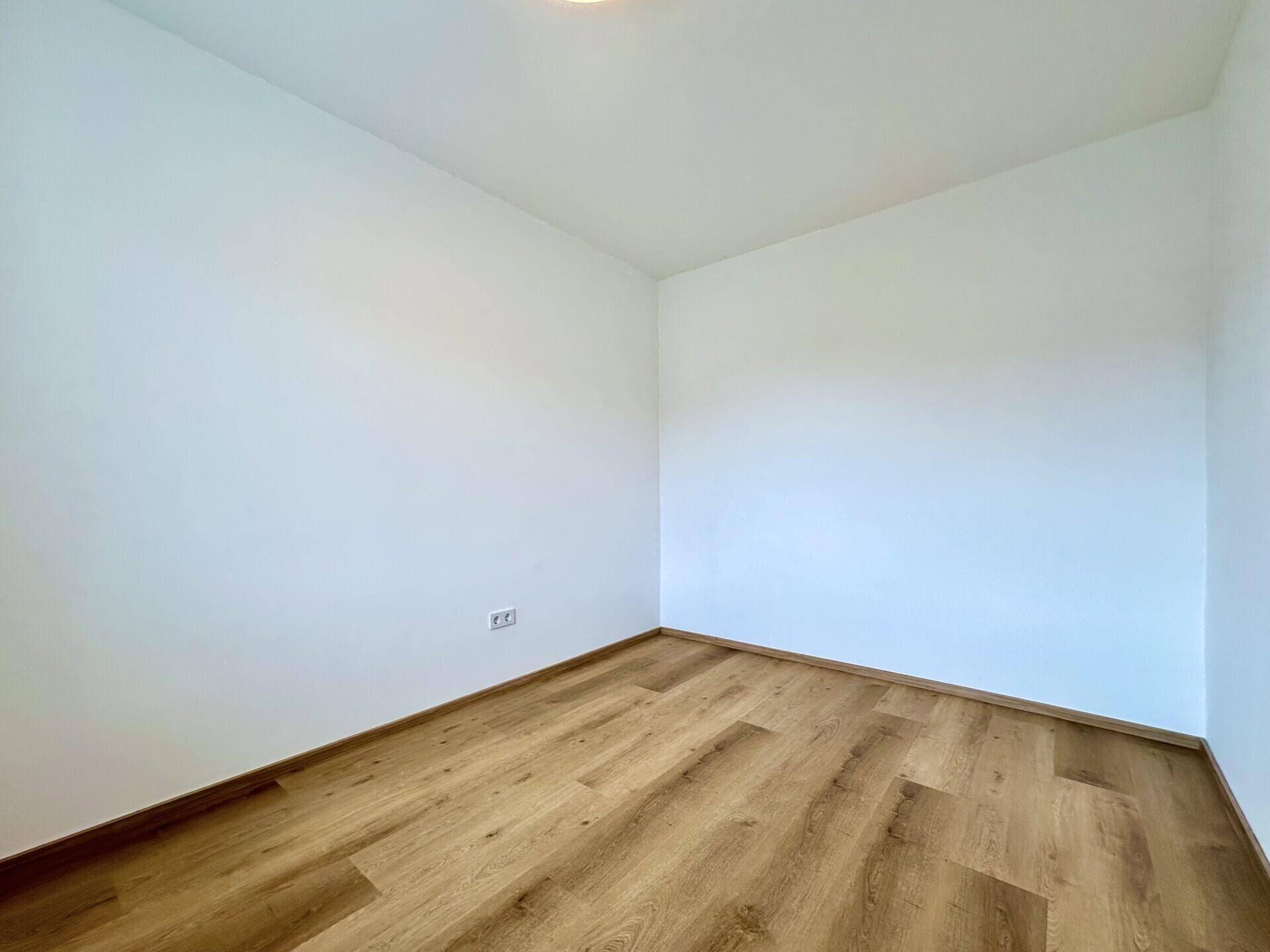 Leerer Raum mit Laminatboden und weißen Wänden, bereit für individuelle Gestaltung.