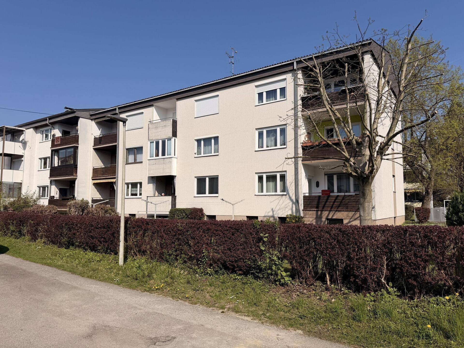 Mehrfamilienhaus mit mehreren Balkonen und gepflegter Außenanlage unter blauem Himmel.