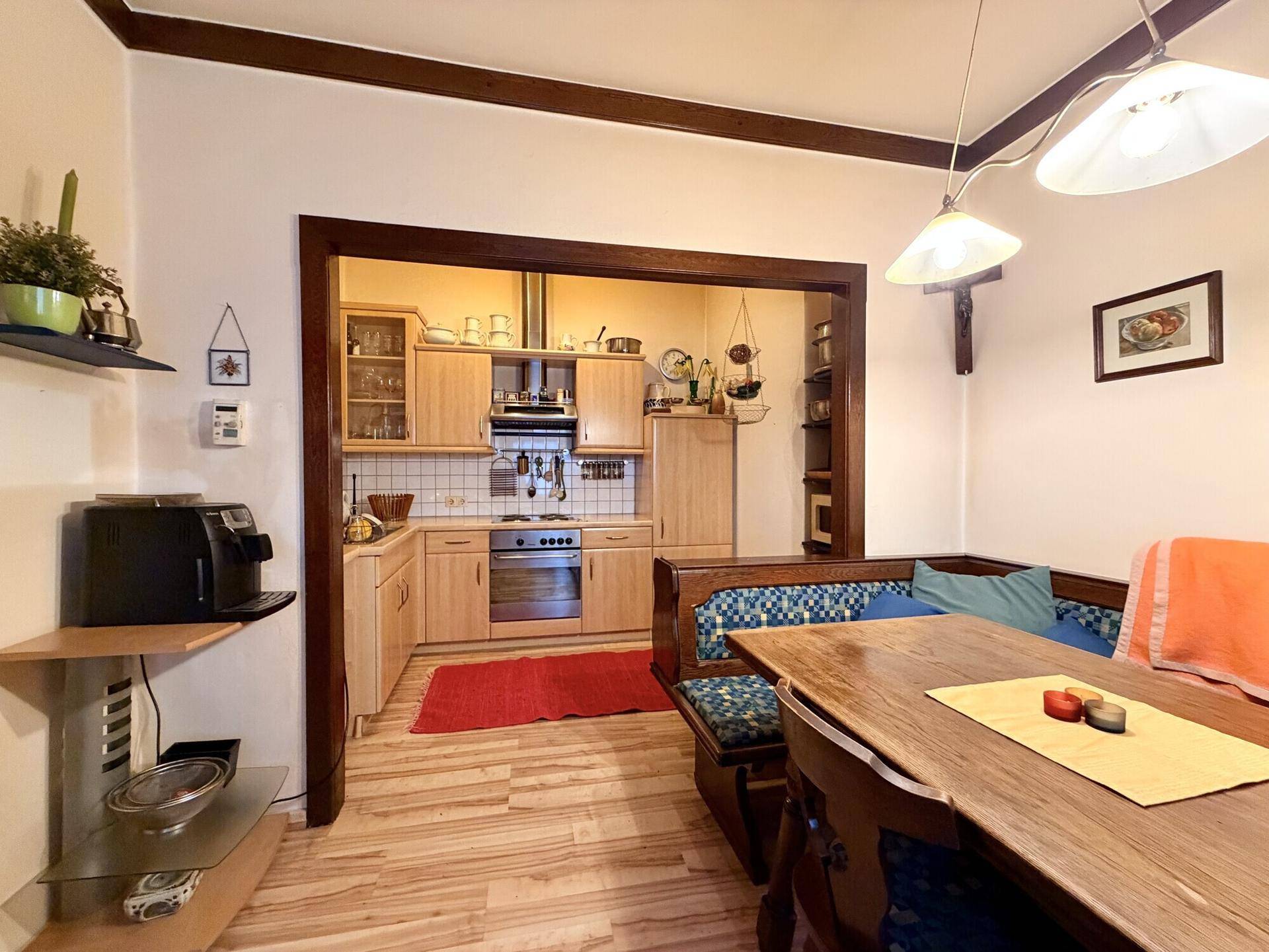 Traditionelle Essecke mit Holztisch und Blick in die helle Küche mit Holzfronten.