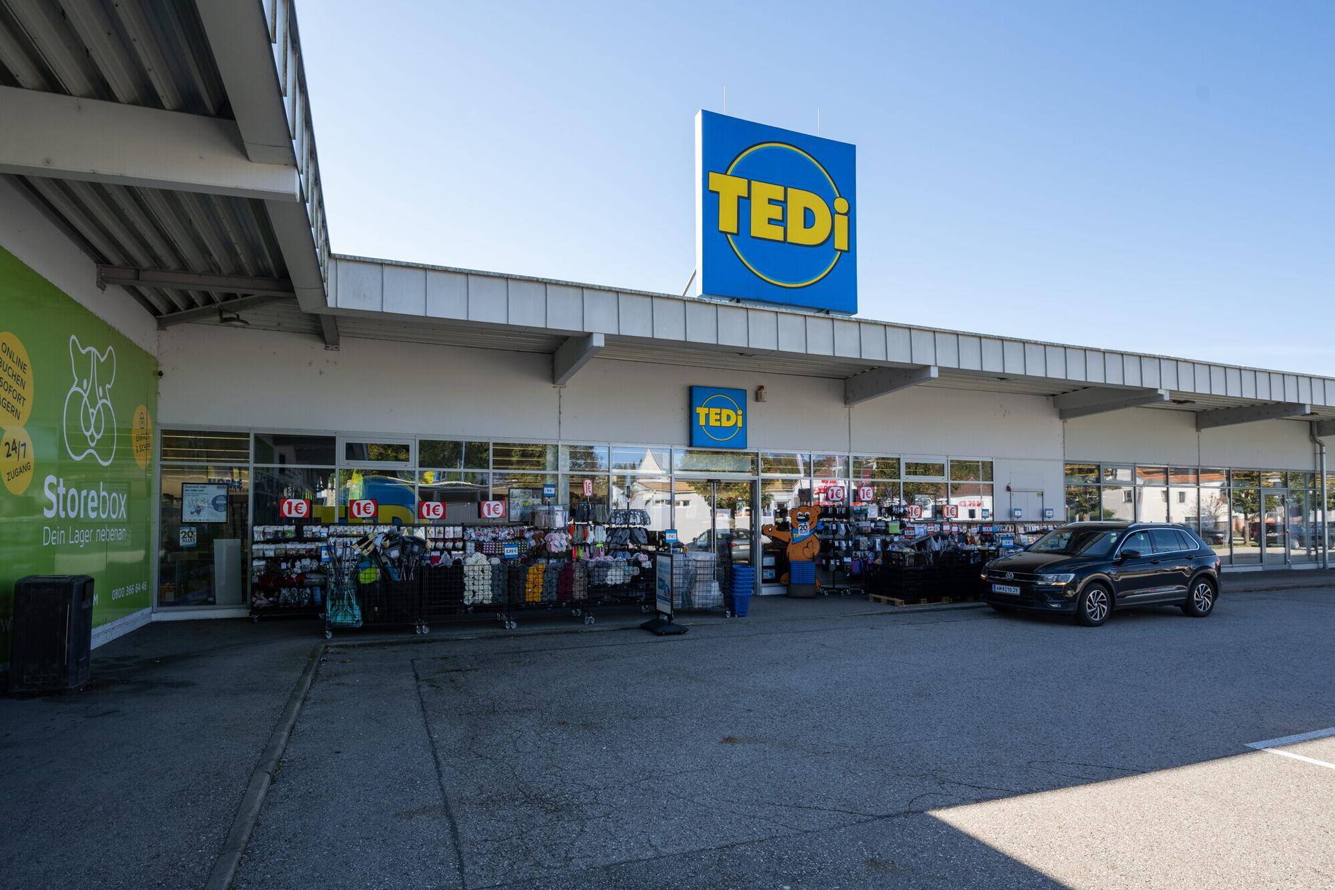 Nahaufnahme des Eingangs einer TEDi-Filiale mit großem Schaufenster und einem geparkten Auto.