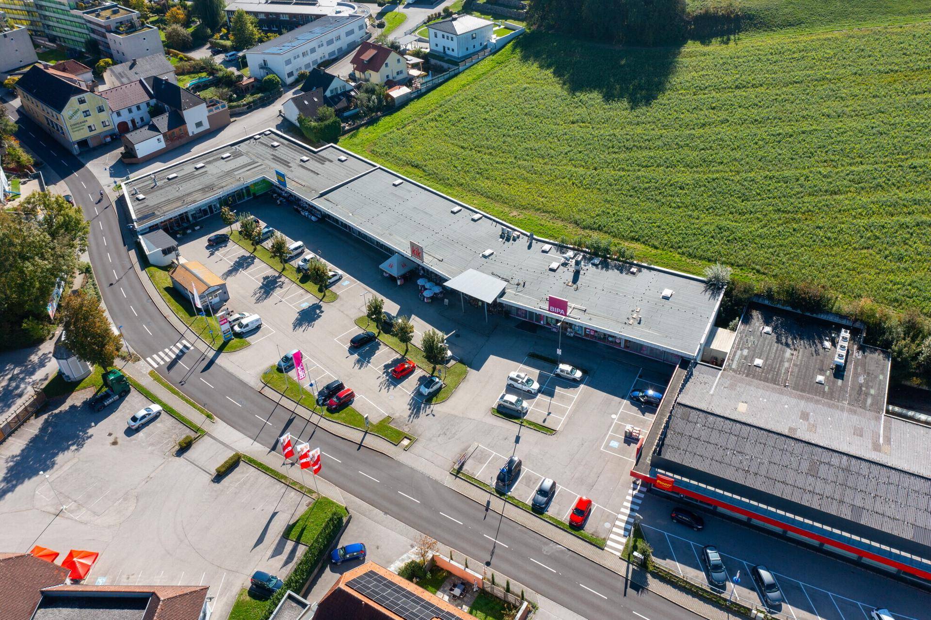Weitläufige Luftansicht eines Geschäftskomplexes mit Parkflächen und angrenzenden Grünflächen.