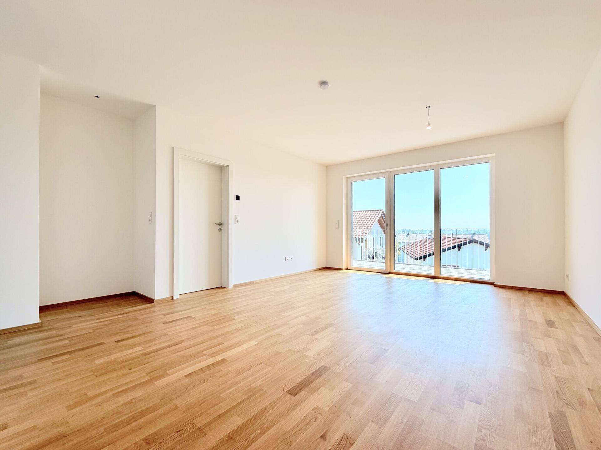 Lichtdurchfluteter Raum mit Holzboden und Schiebetüren zum Balkon, bietet einen schönen Ausblick.