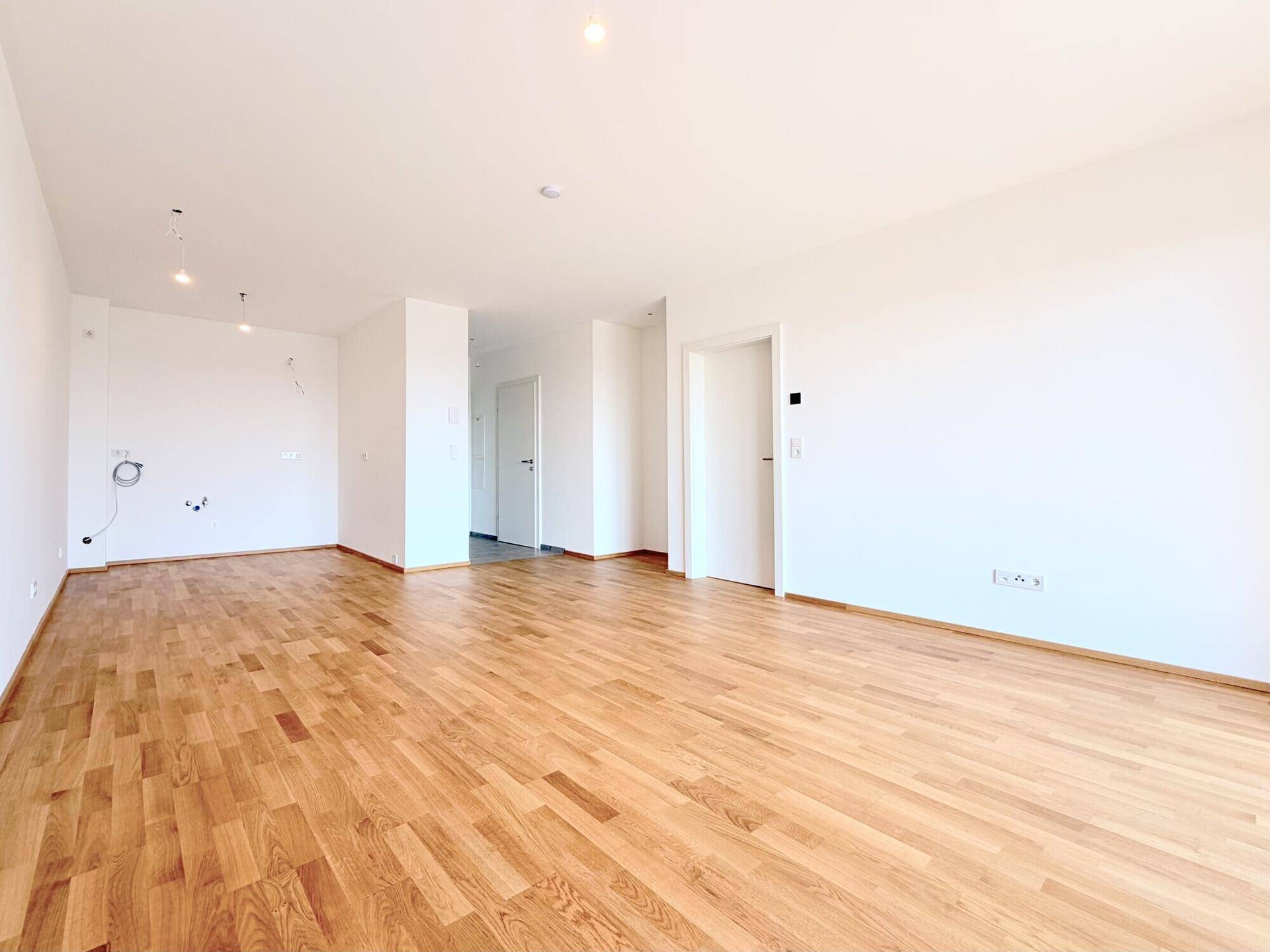 Geräumiger, heller Raum mit Holzboden und mehreren Türen, bietet flexible Gestaltungsmöglichkeiten.