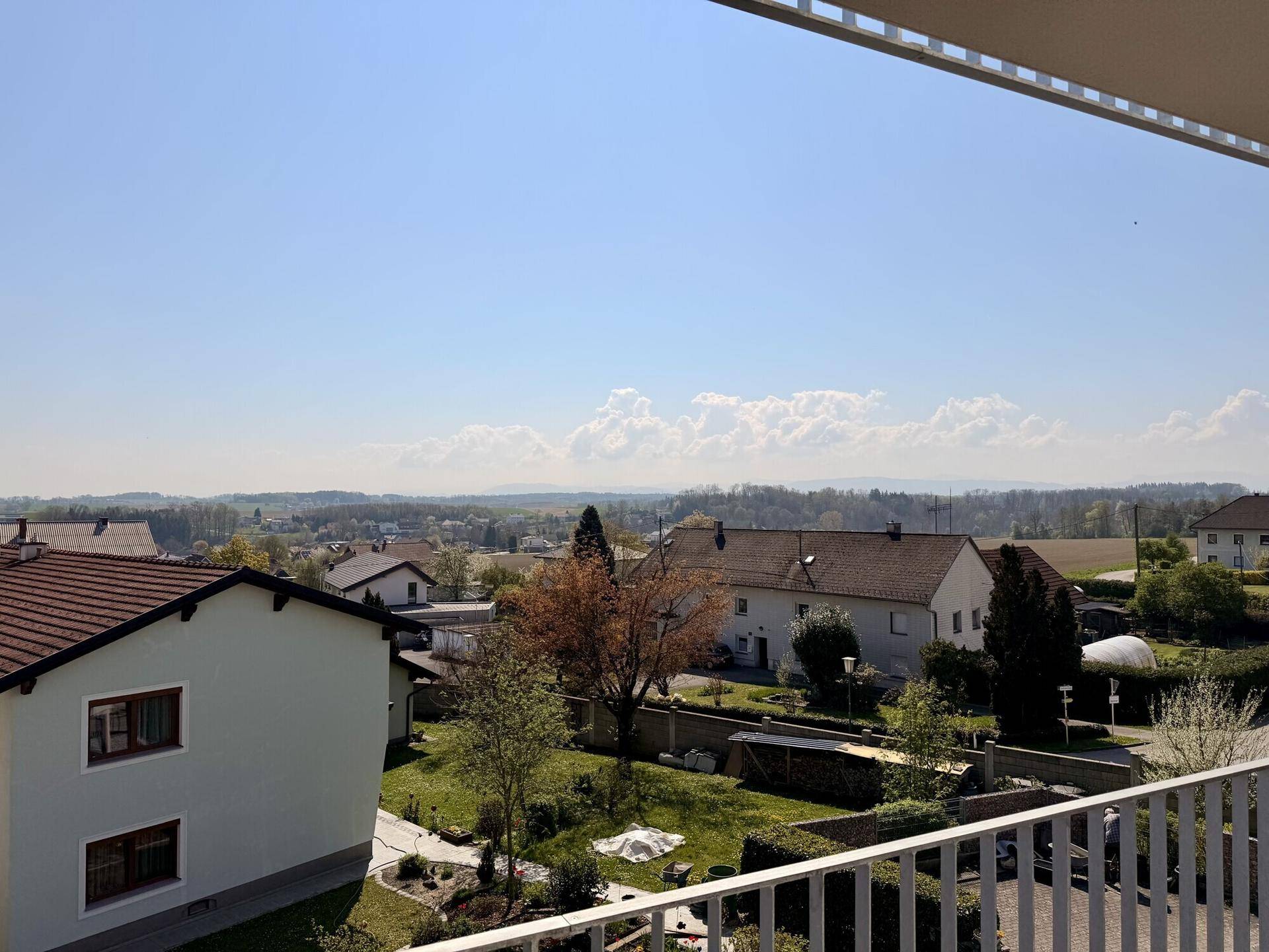 Weitläufiger Blick vom Balkon über die Dächer der Häuser und die grüne Landschaft.