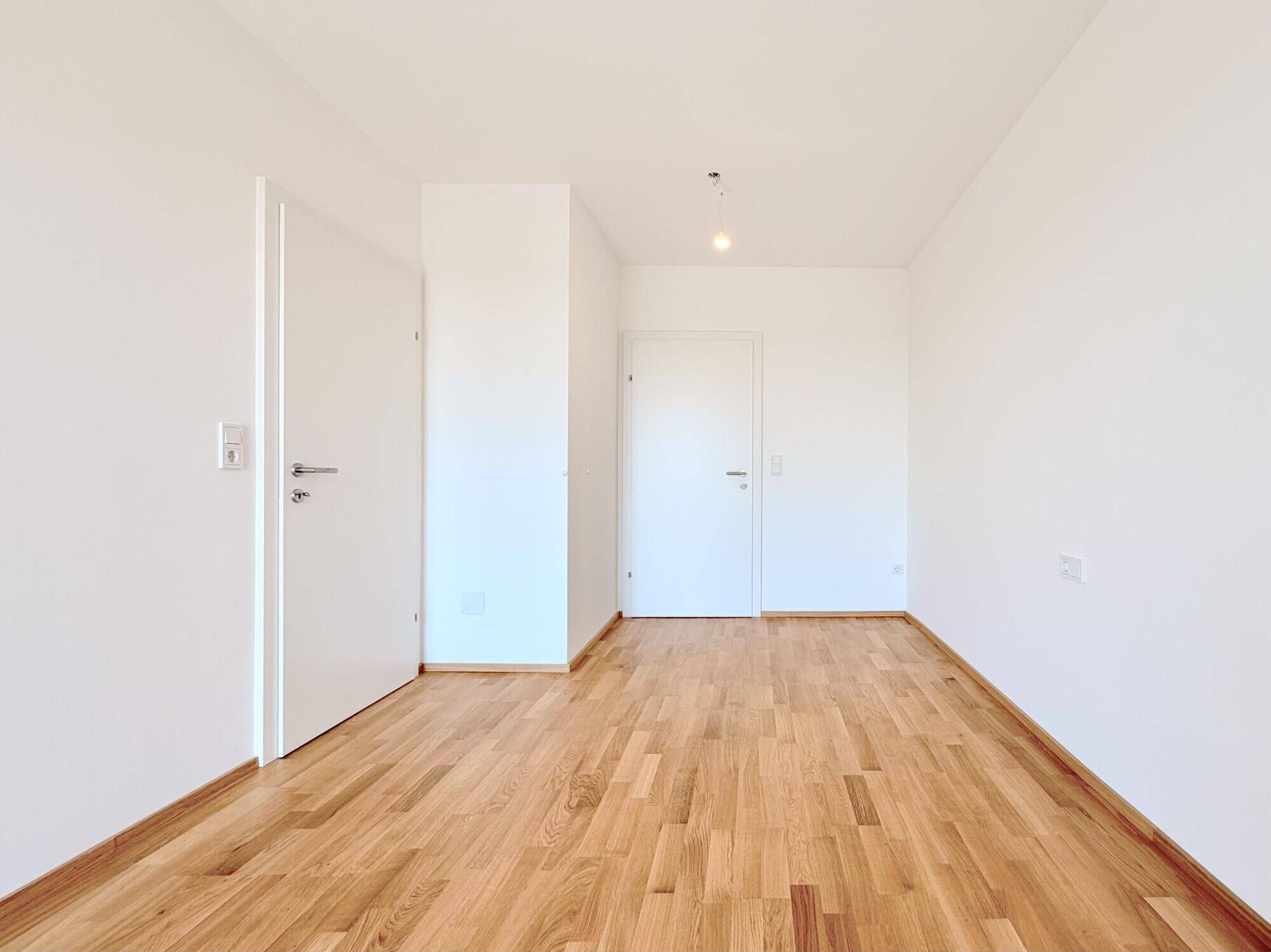 Heller Flur mit Holzboden und zwei Türen, der verschiedene Räume miteinander verbindet.