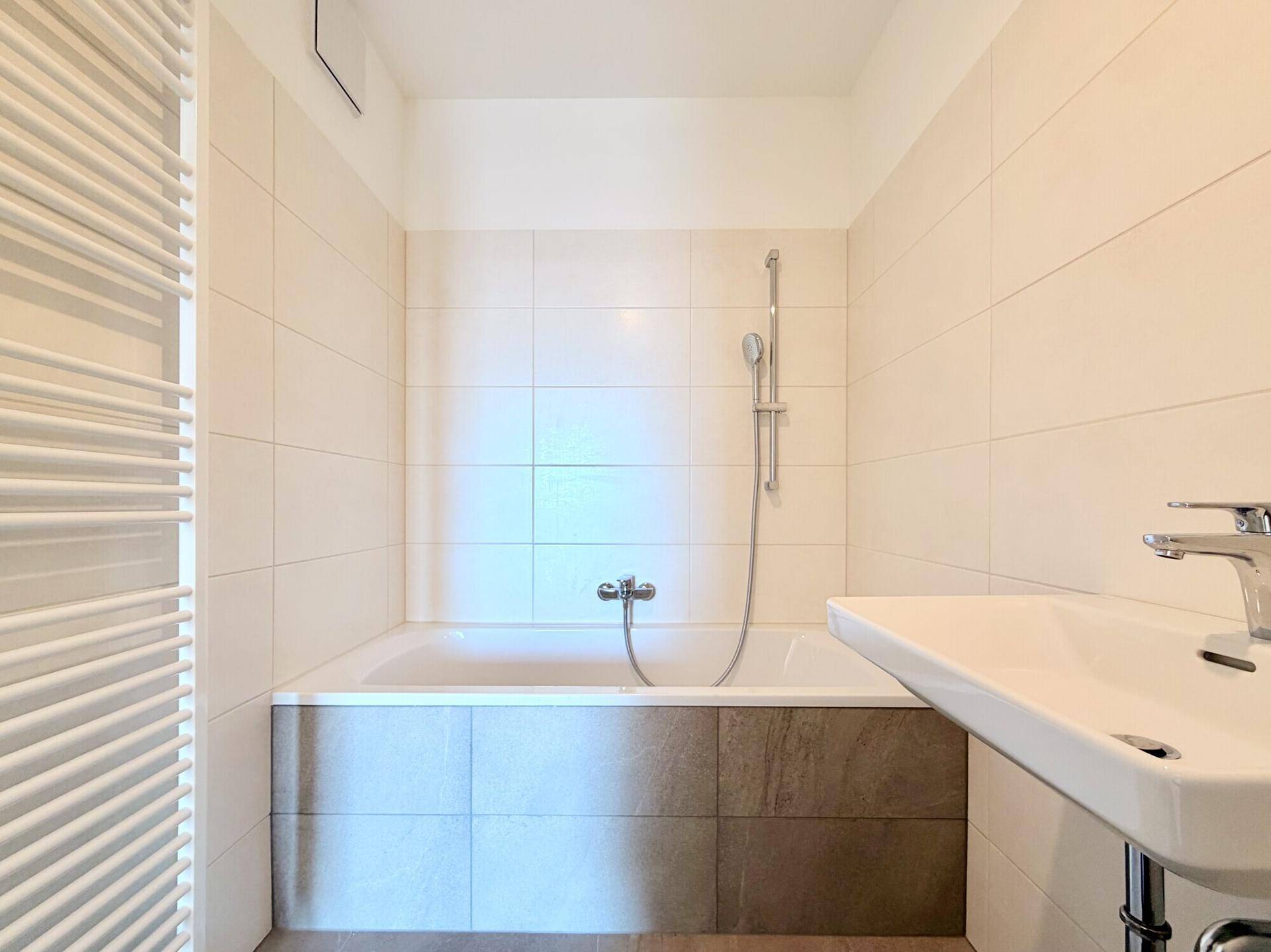 Helles Badezimmer mit Badewanne und modernem Waschbecken, ausgestattet mit hellen Wandfliesen.