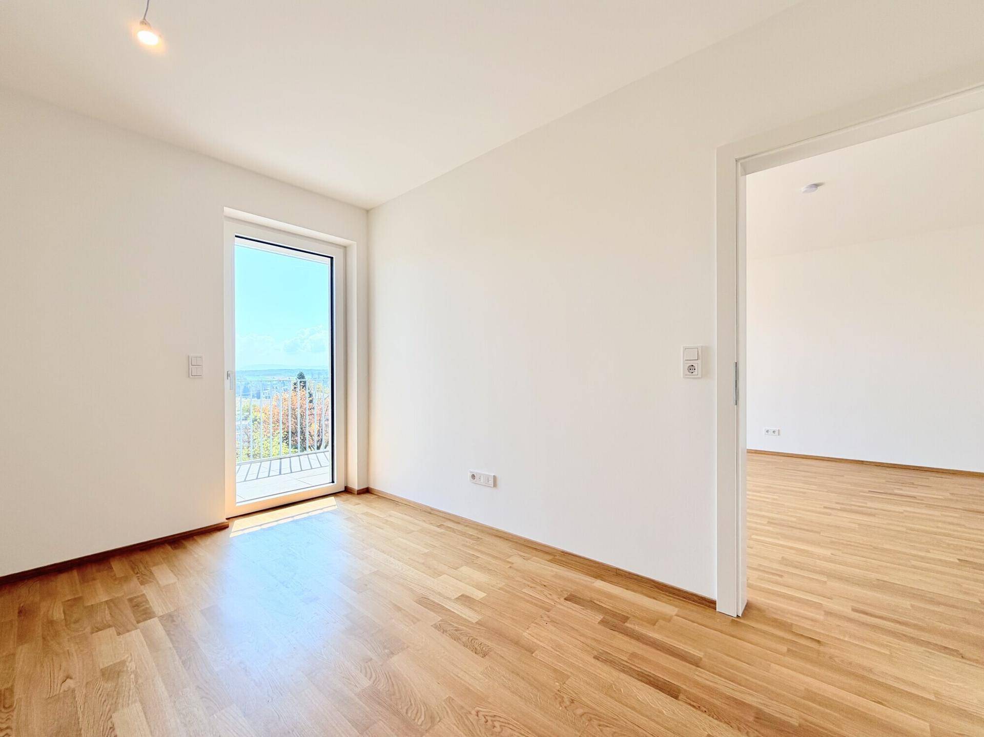 Helles Zimmer mit Holzboden und Zugang zu einem kleinen Balkon, ideal als Schlaf- oder Arbeitszimmer.