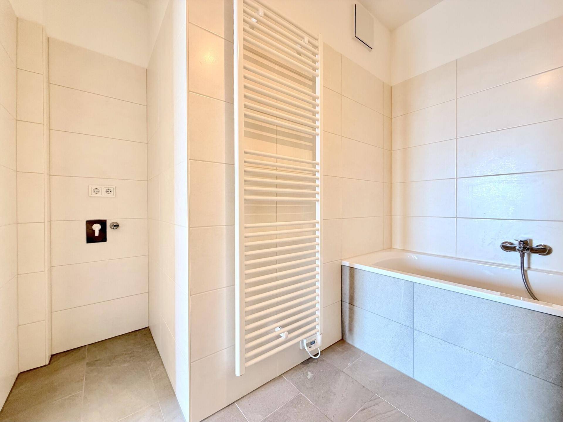 Modernes Badezimmer mit beheiztem Handtuchhalter und Platz für eine Toilette, hell gefliest.