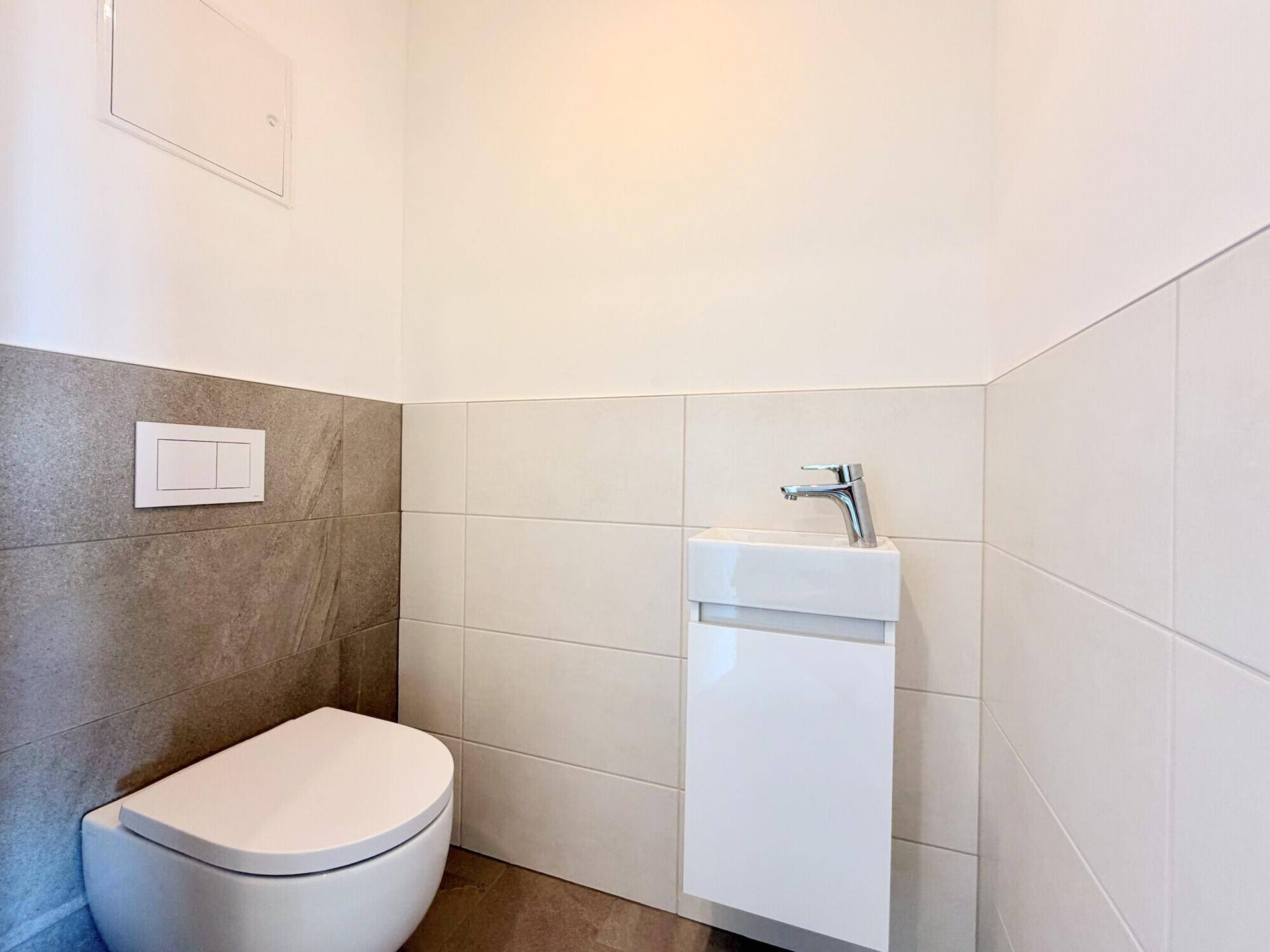 Modernes Gäste-WC mit wandhängender Toilette und kleinem Waschbecken, hell gefliest.