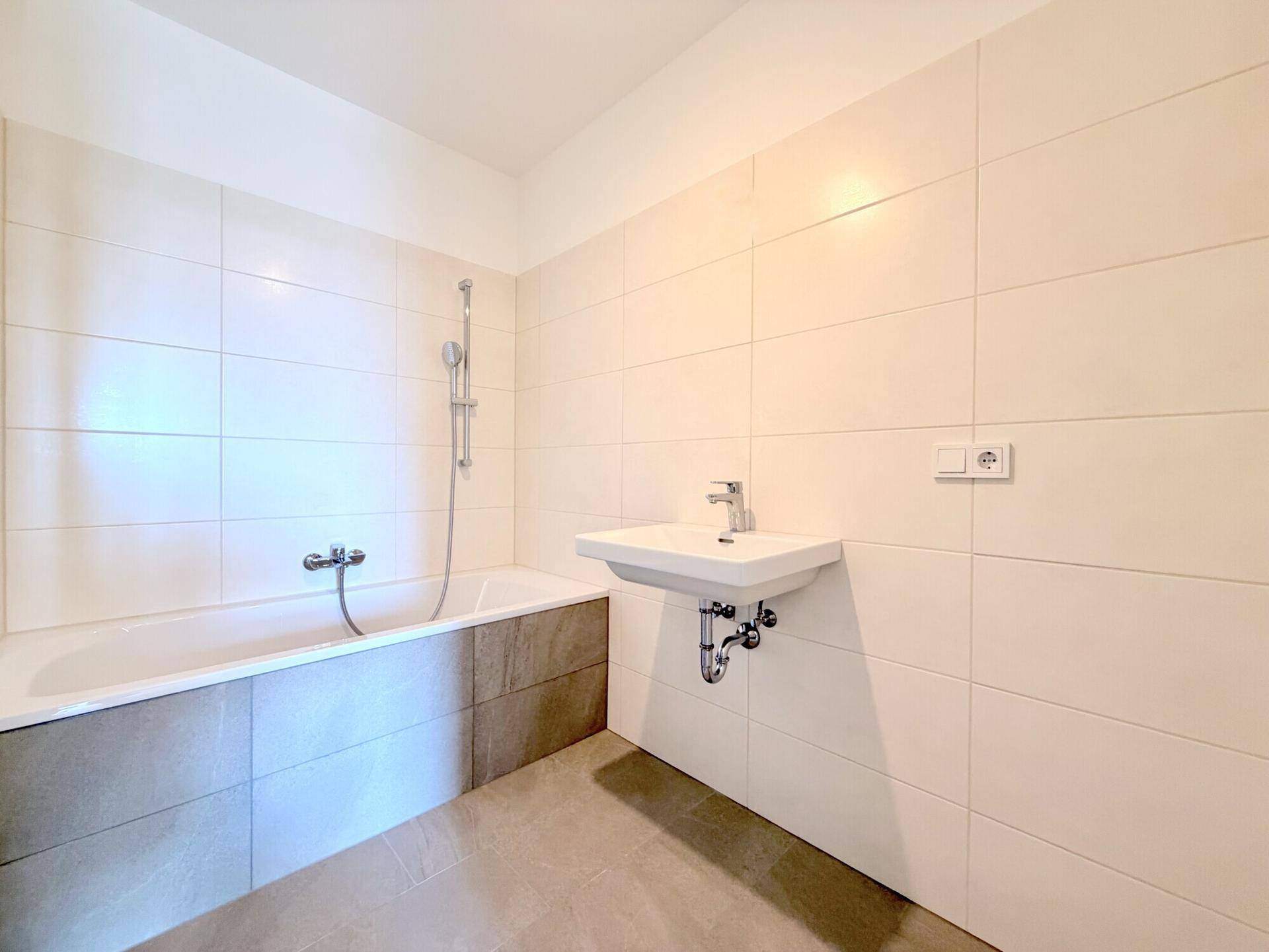 Modernes Badezimmer mit Badewanne, Waschbecken und hellen Fliesen an Wänden und Boden.