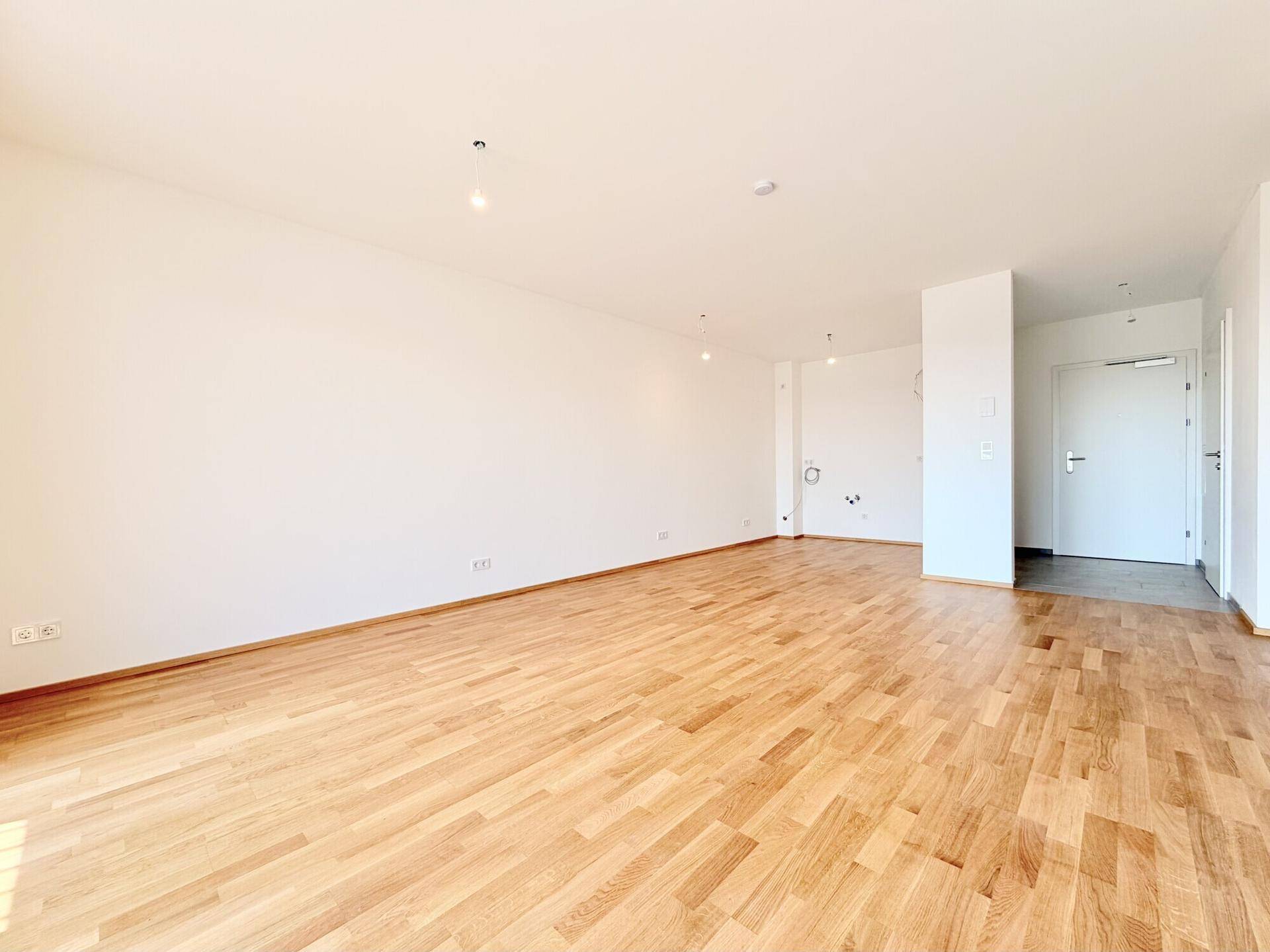 Geräumiger, heller Raum mit Holzboden und Zugang zum Eingangsbereich, ideal für offenes Wohnen.