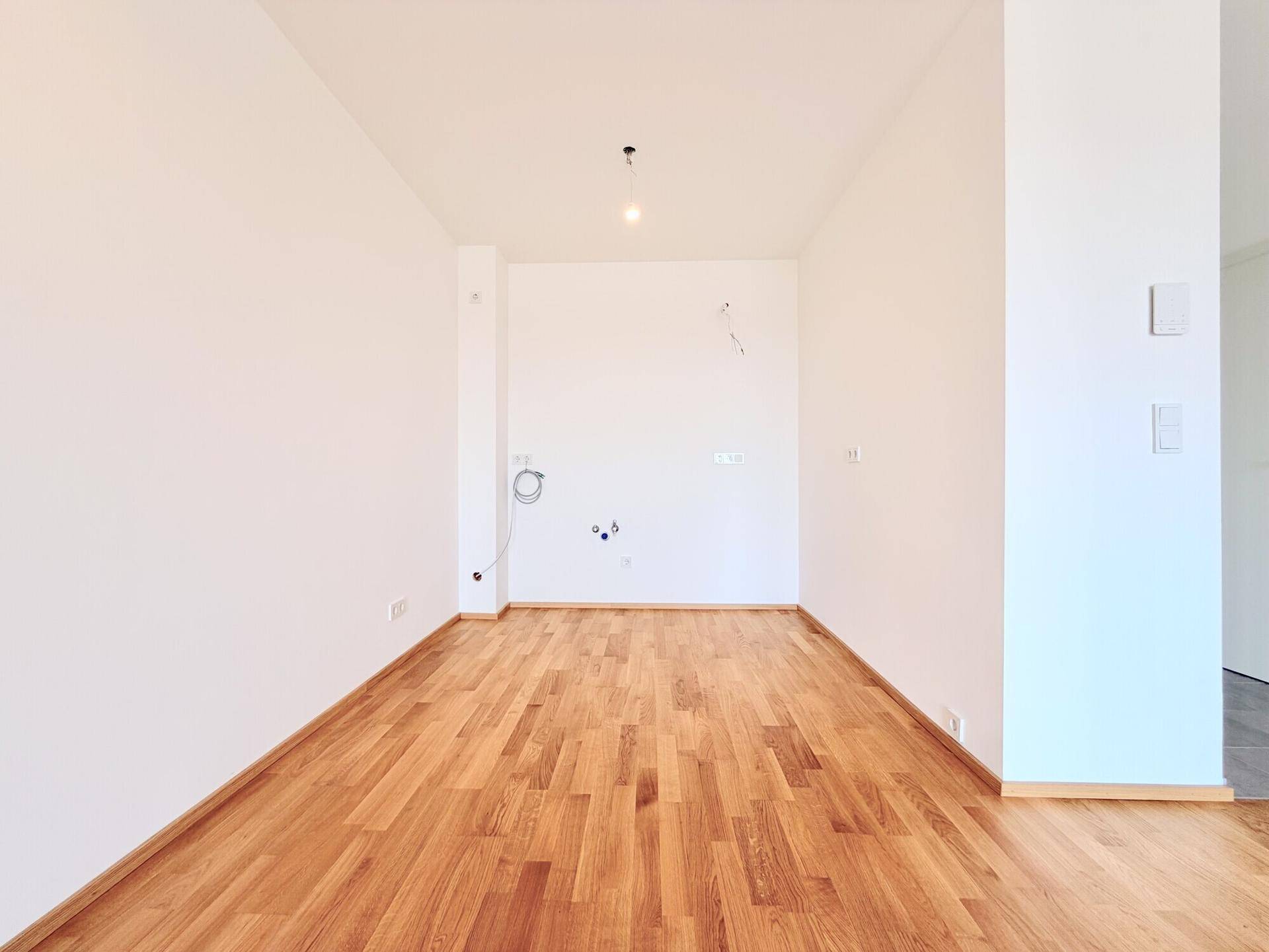 Heller Raum mit Holzboden und vorbereiteten Wandanschlüssen, ideal für eine individuelle Einrichtung.