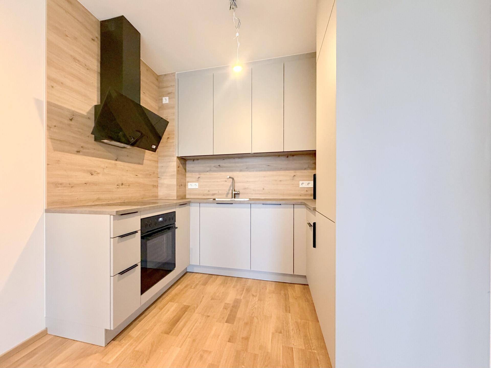 Moderne Einbauküche mit hellgrauen Fronten, Holzakzenten und integriertem Backofen in einem Neubau.