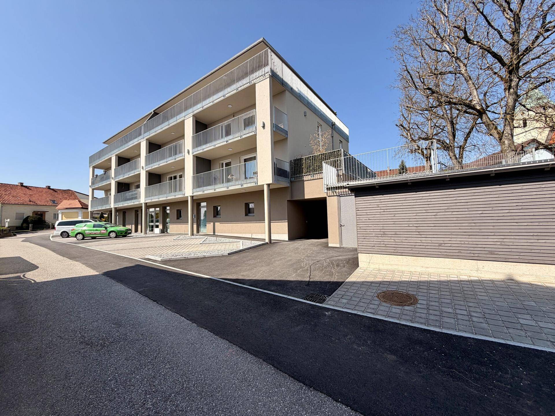 Außenansicht eines modernen Mehrfamilienhauses mit Parkplätzen und Zufahrt zur Tiefgarage.