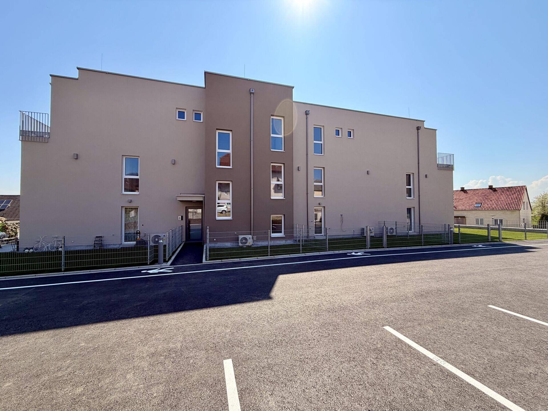 Rückansicht eines modernen Mehrfamilienhauses mit Parkplätzen und gepflegter Außenanlage.