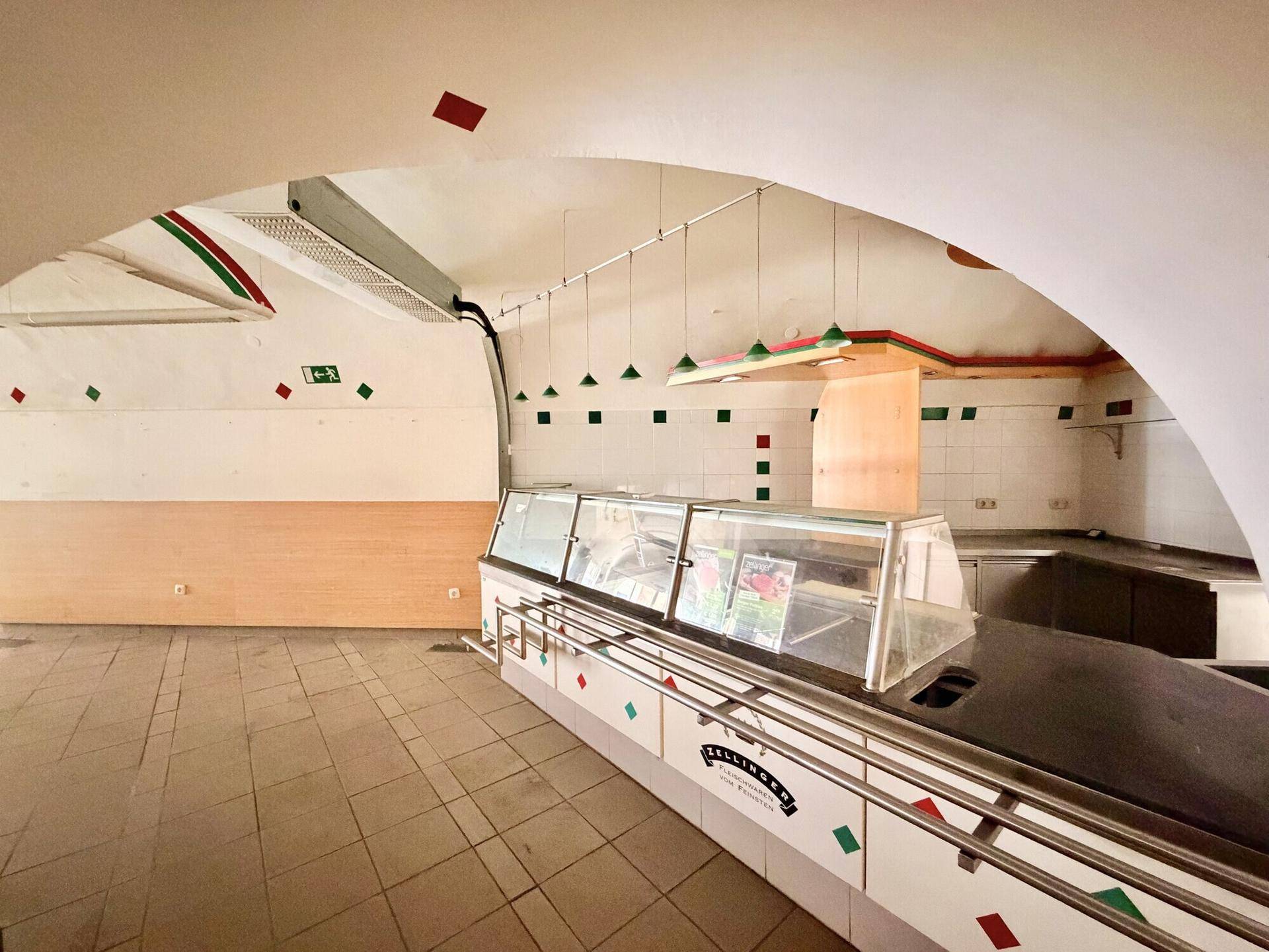 Großer Raum mit Gewölbedecken, gefliesten Wänden und einer langen Theke, ideal für Gastronomie oder Verkauf.