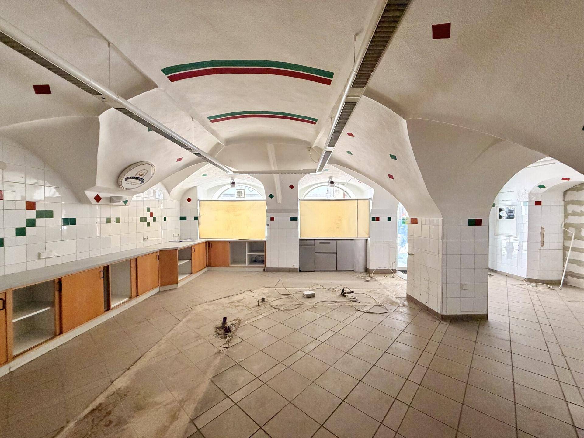 Geräumiger Bereich mit Gewölbedecken, gefliesten Wänden und Arbeitsflächen, vorbereitet für eine gewerbliche Nutzung.
